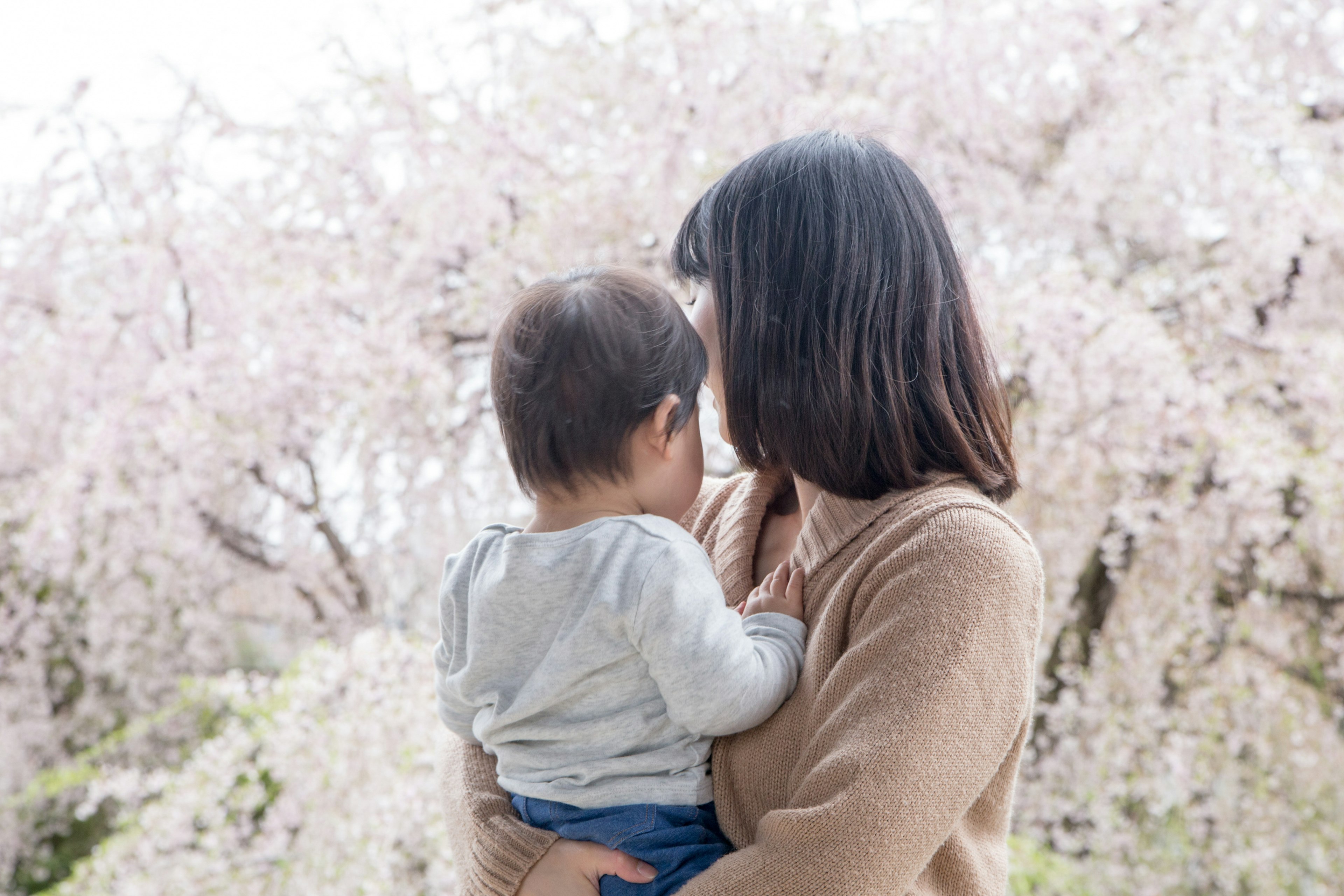 Una madre che tiene un bambino davanti a alberi di ciliegio in fiore