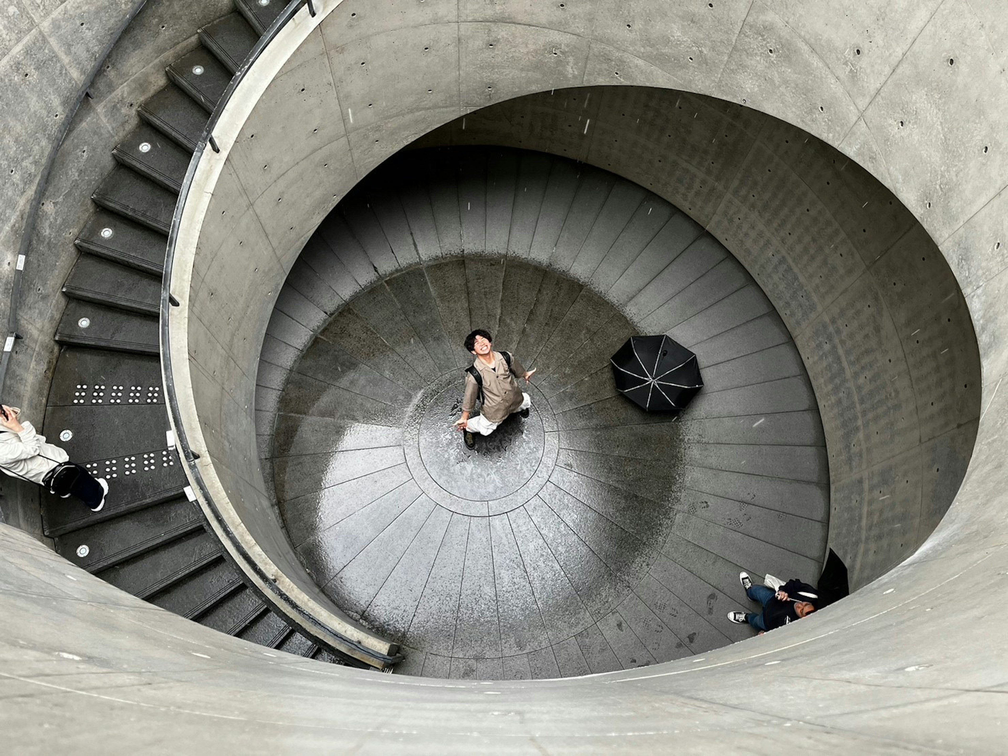 A modern concrete space viewed from above featuring a spiral staircase and a person standing