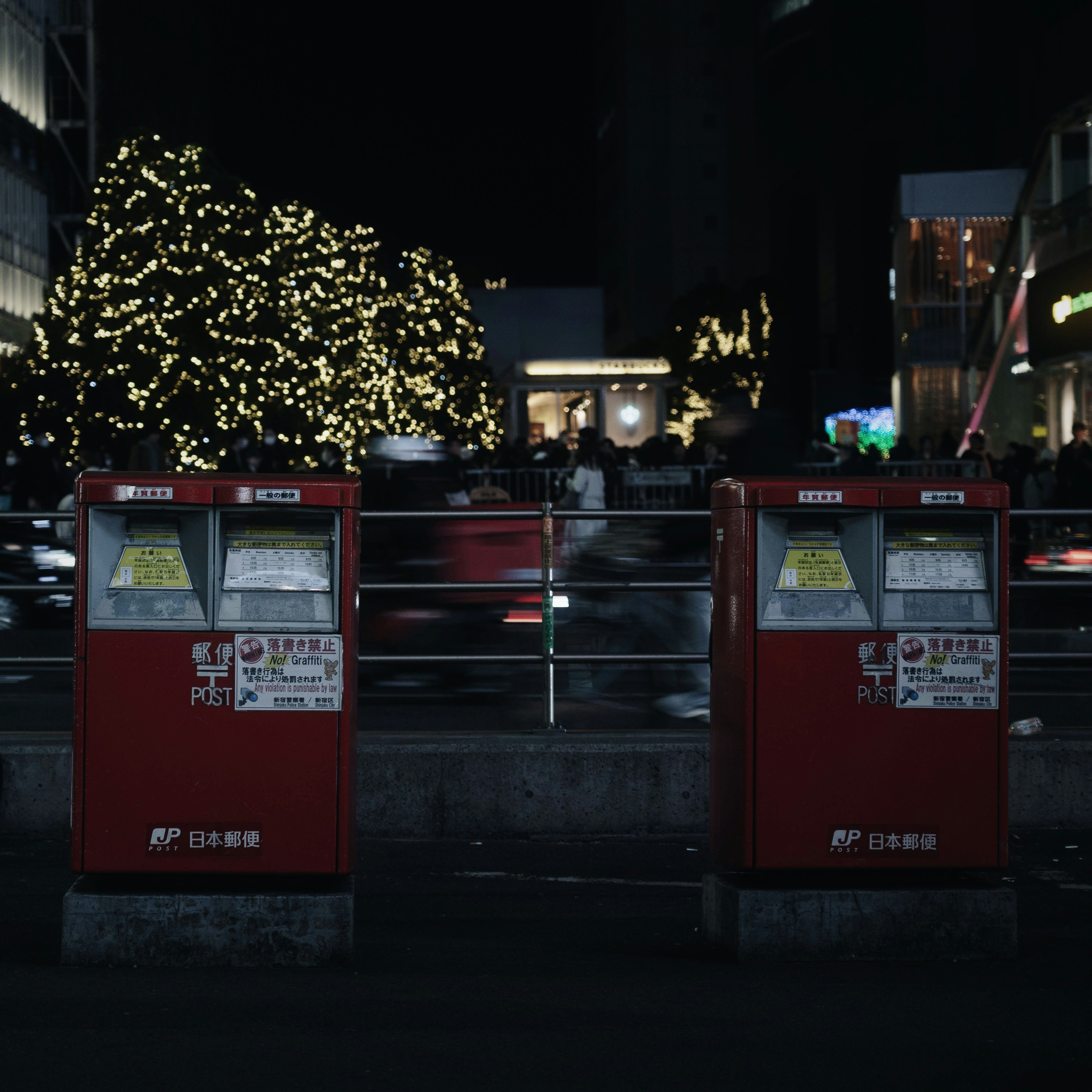 Red mailboxes standing in a nighttime city scene with illuminated trees