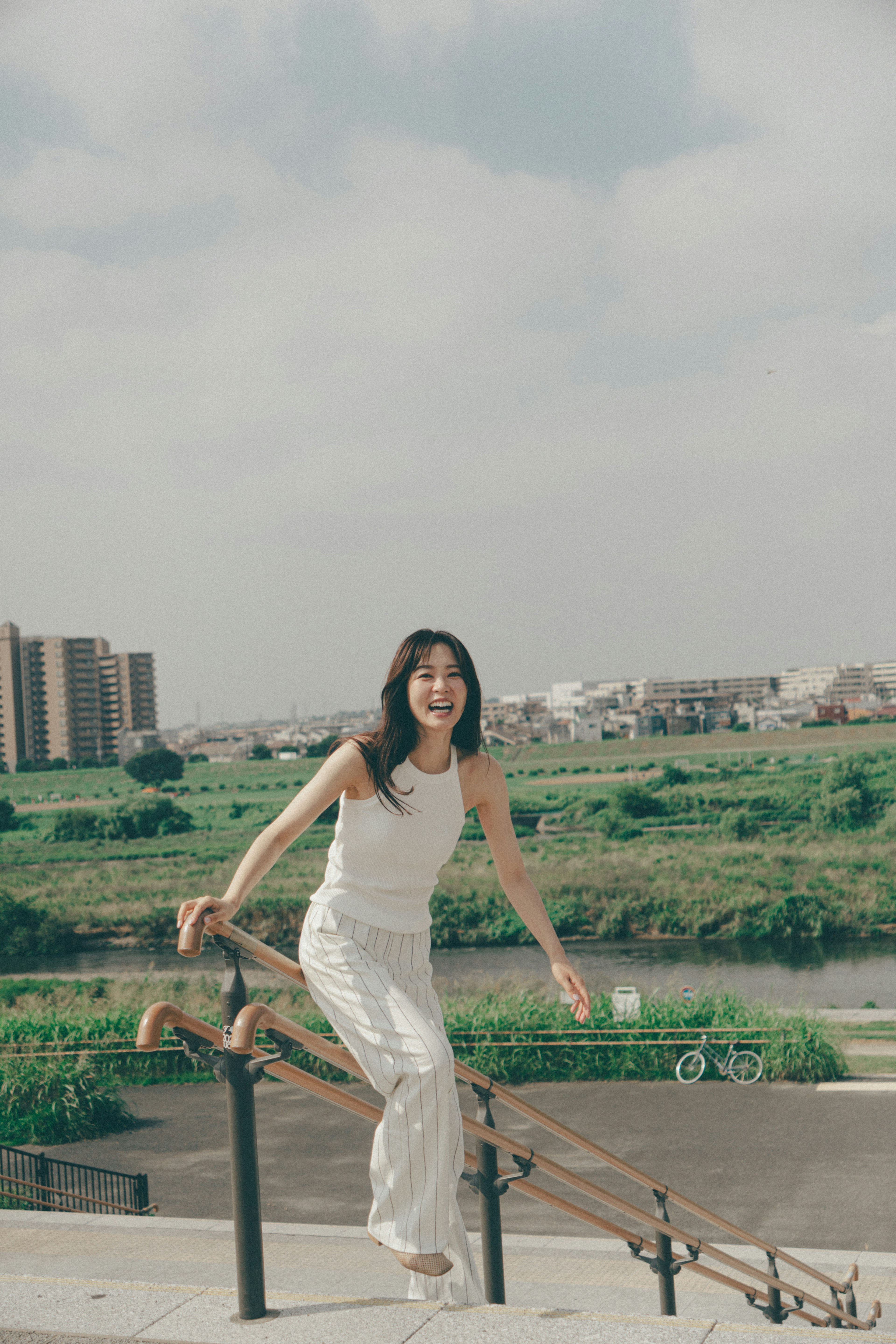 A woman in a white dress joyfully standing near a river in a scenic landscape