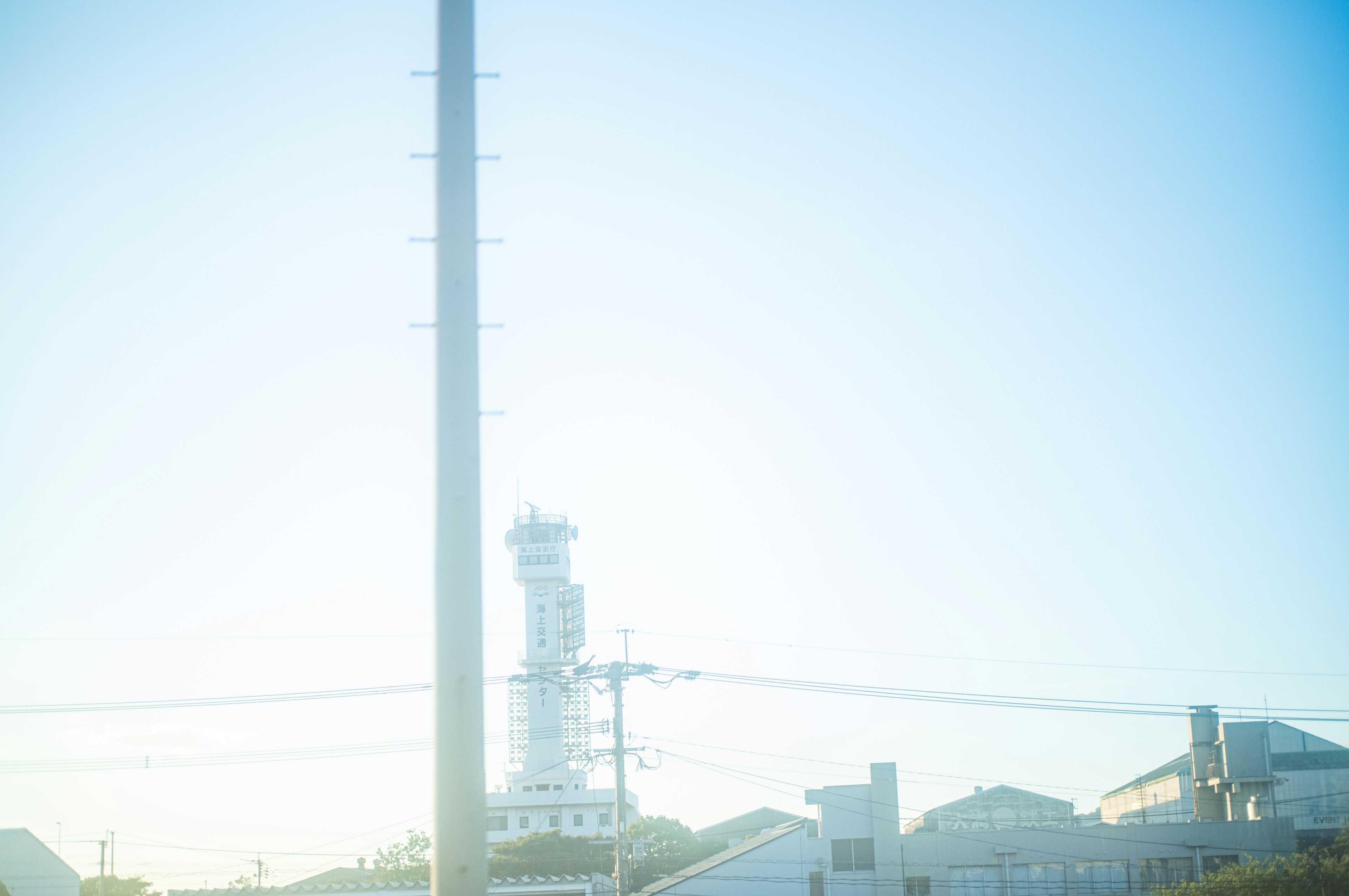 青空の下に高い電柱と灯台が見える風景