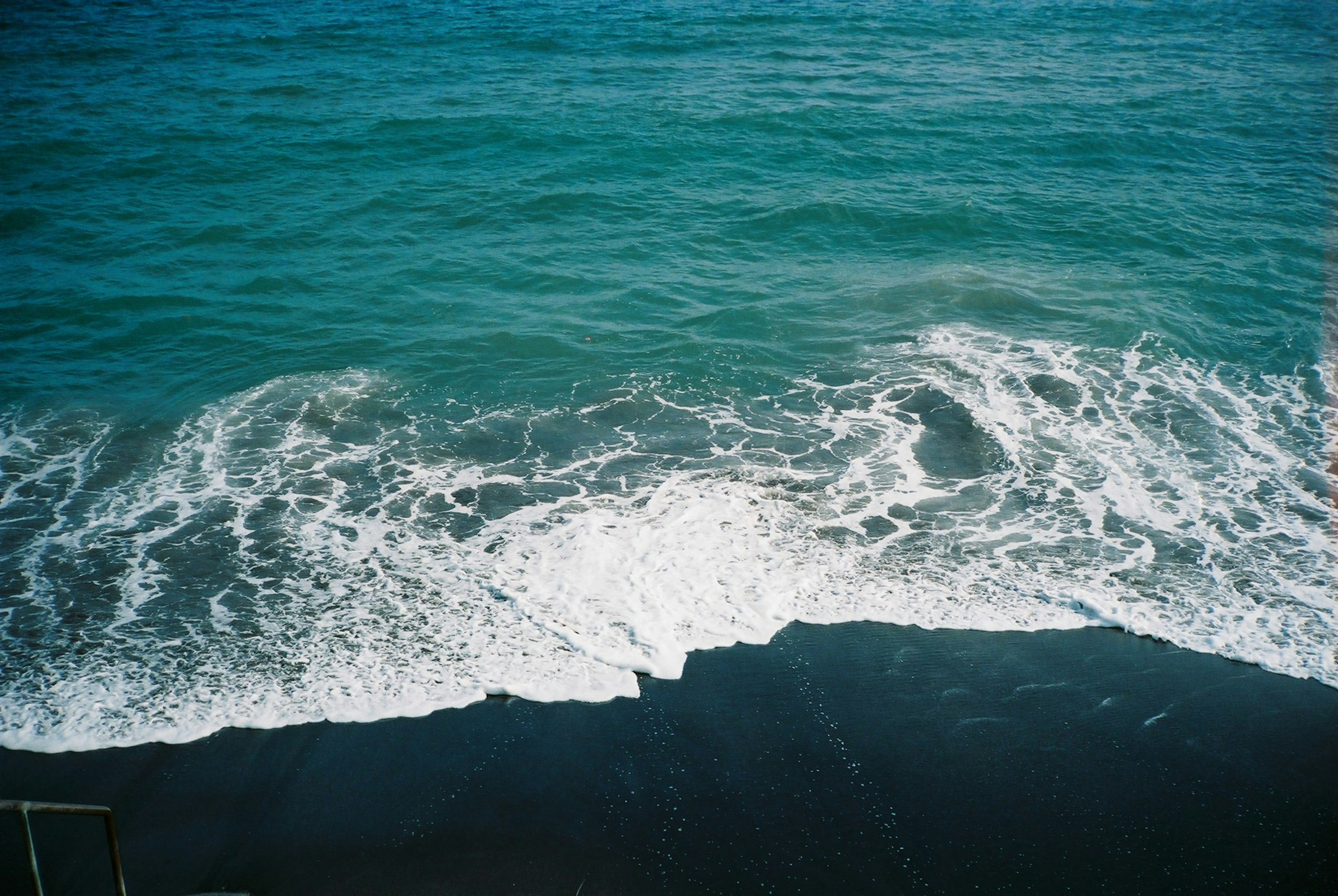 Blue ocean waves crashing onto a dark shoreline