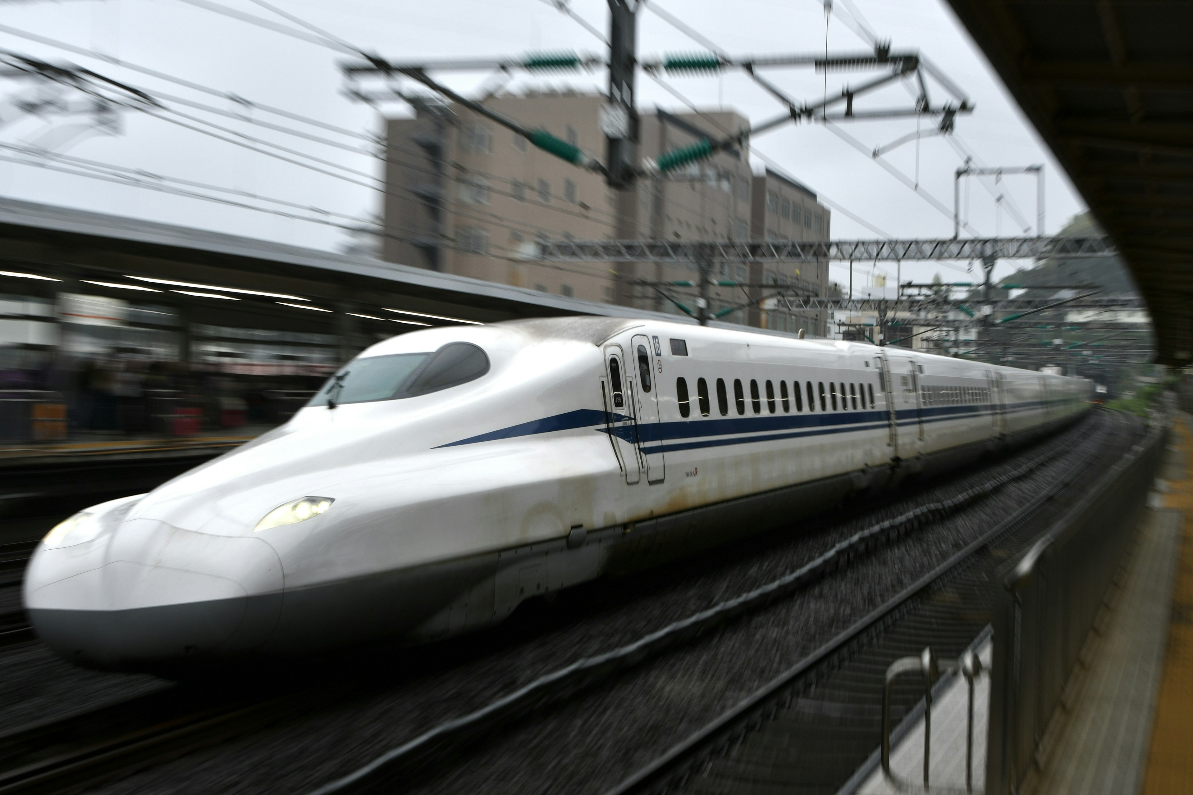 Shinkansen pasando por una estación en un día lluvioso