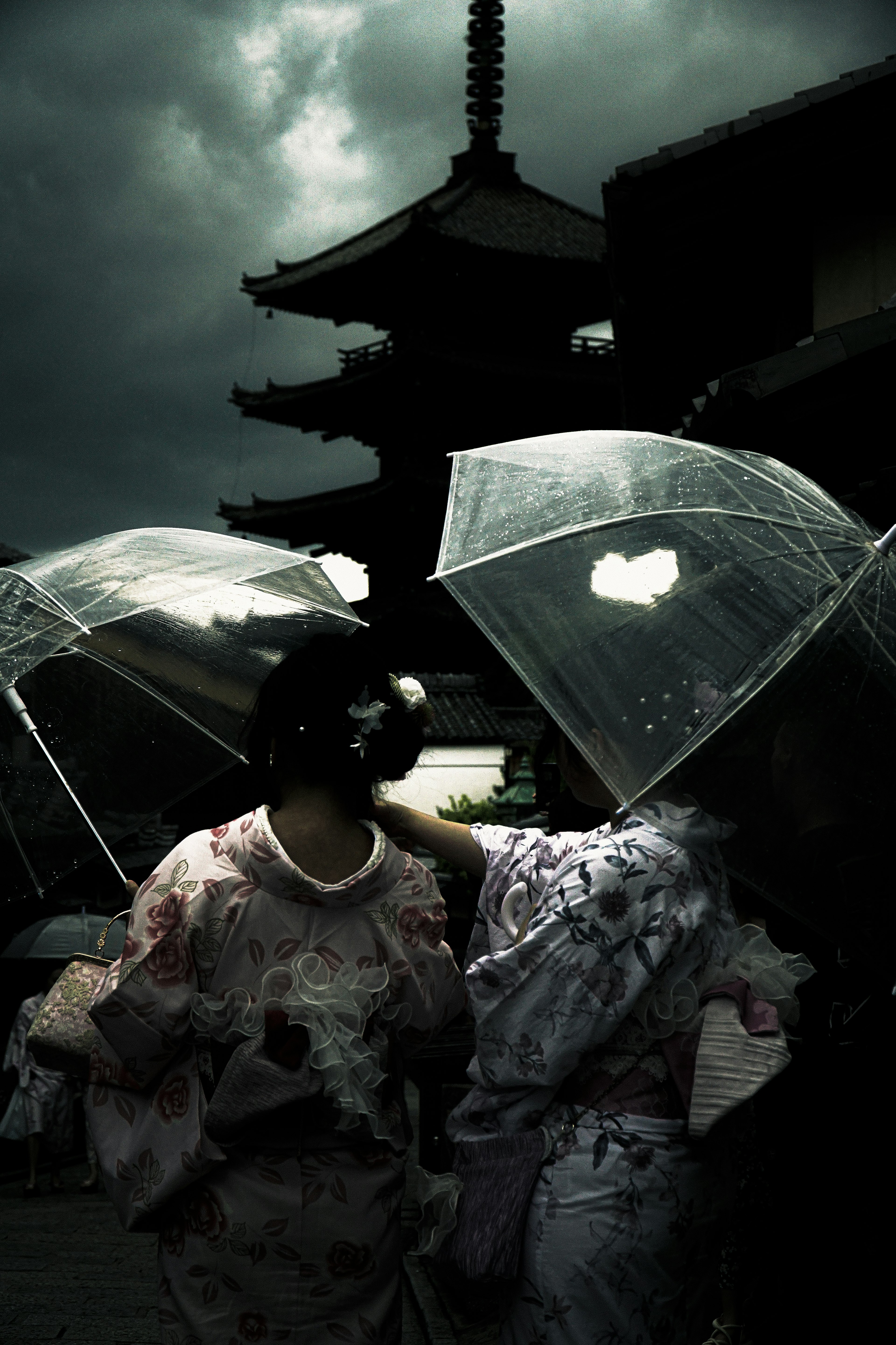 Mujeres en kimonos sosteniendo paraguas transparentes bajo un cielo oscuro con una pagoda al fondo