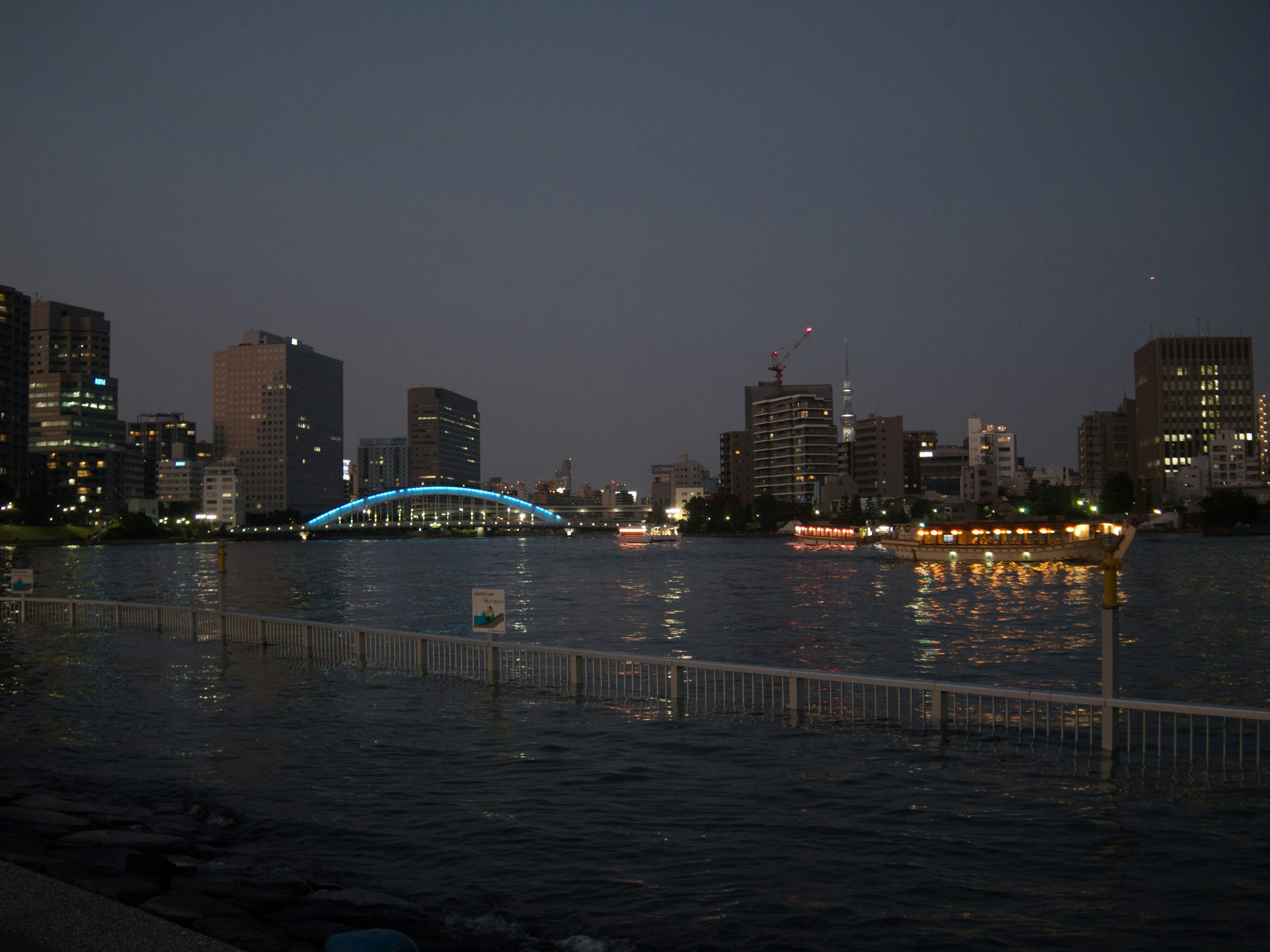 Paisaje urbano nocturno con edificios iluminados y un puente brillante sobre el río