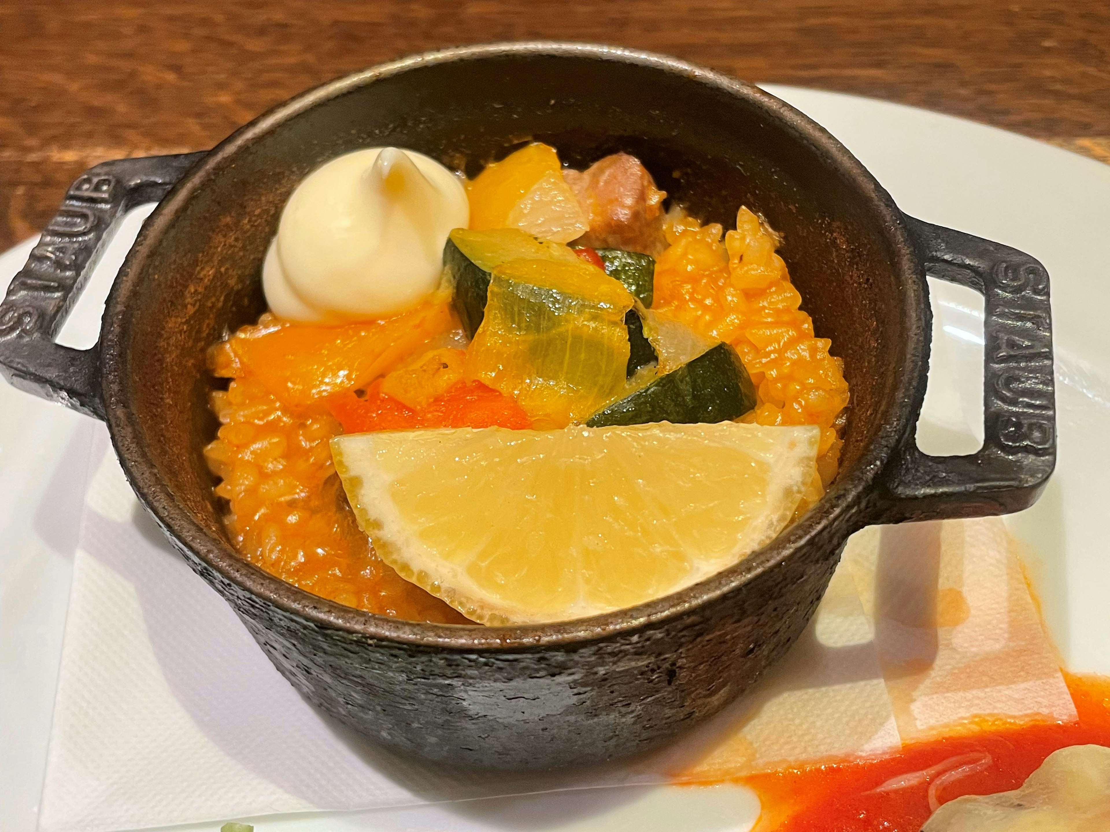 Plat de riz coloré servi dans une petite casserole en fonte avec des légumes et une tranche de citron