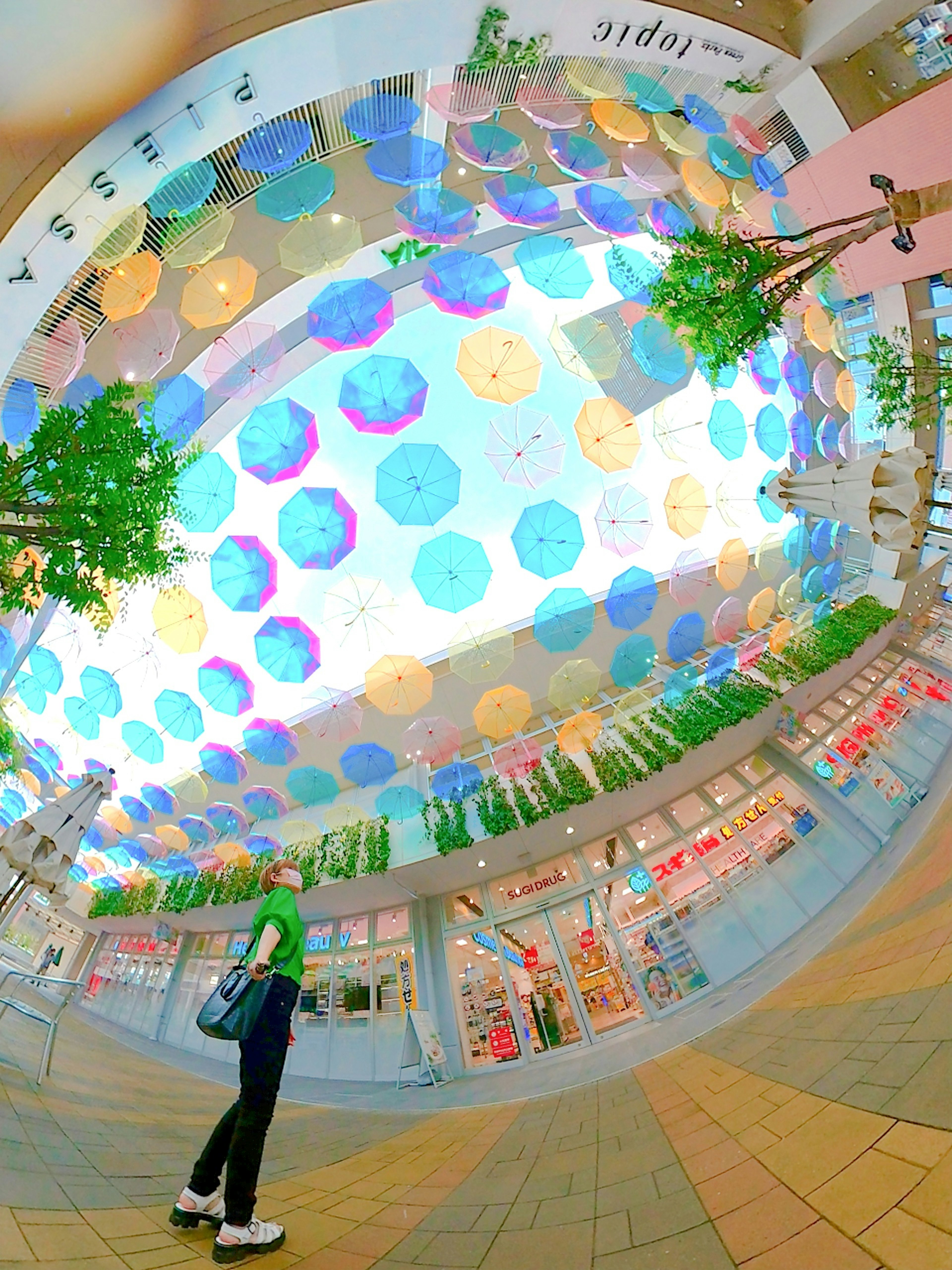 A person standing in a shopping mall with colorful umbrellas hanging from the ceiling