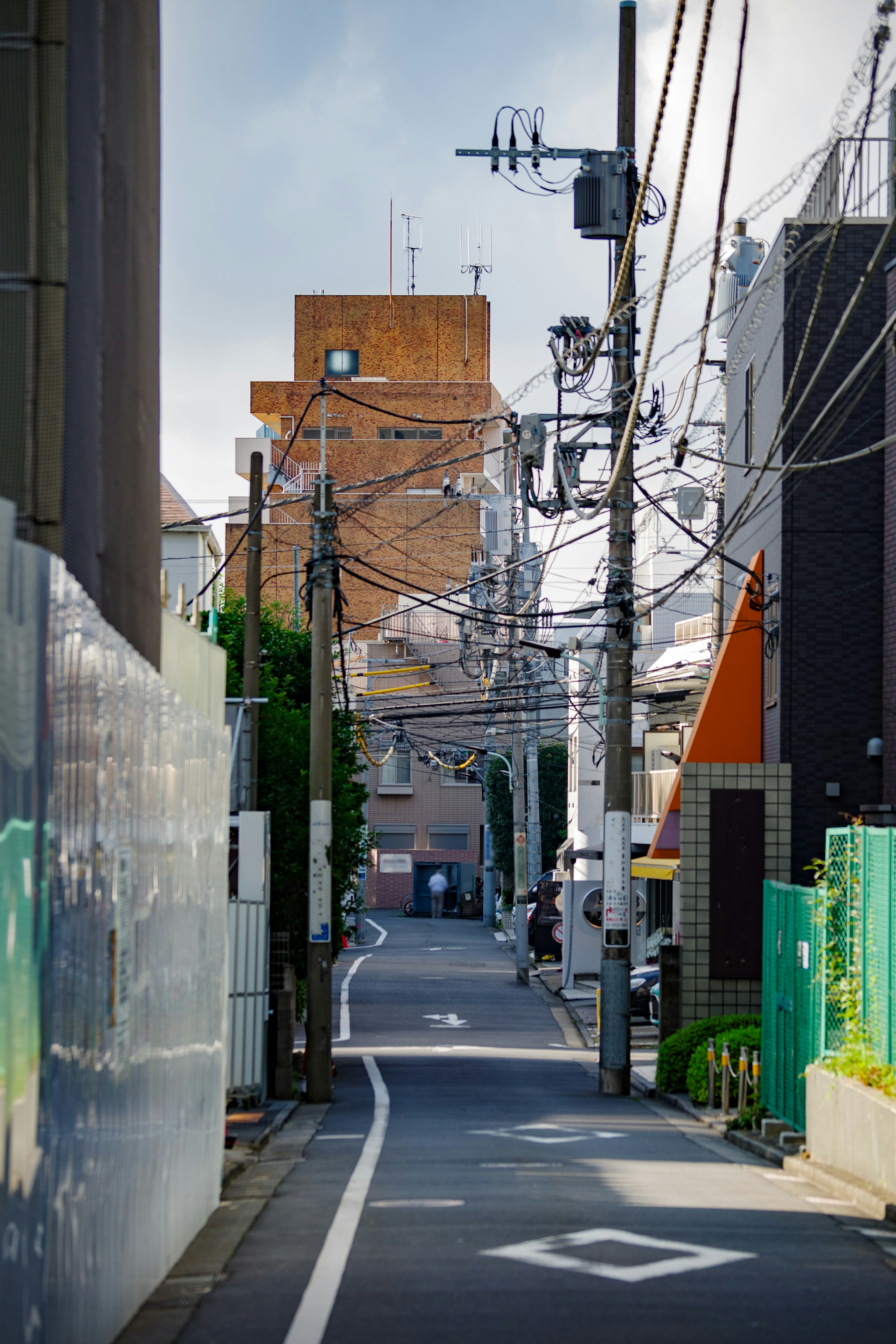 Narrow alleyway with intersecting power lines residential buildings and a distant orange structure