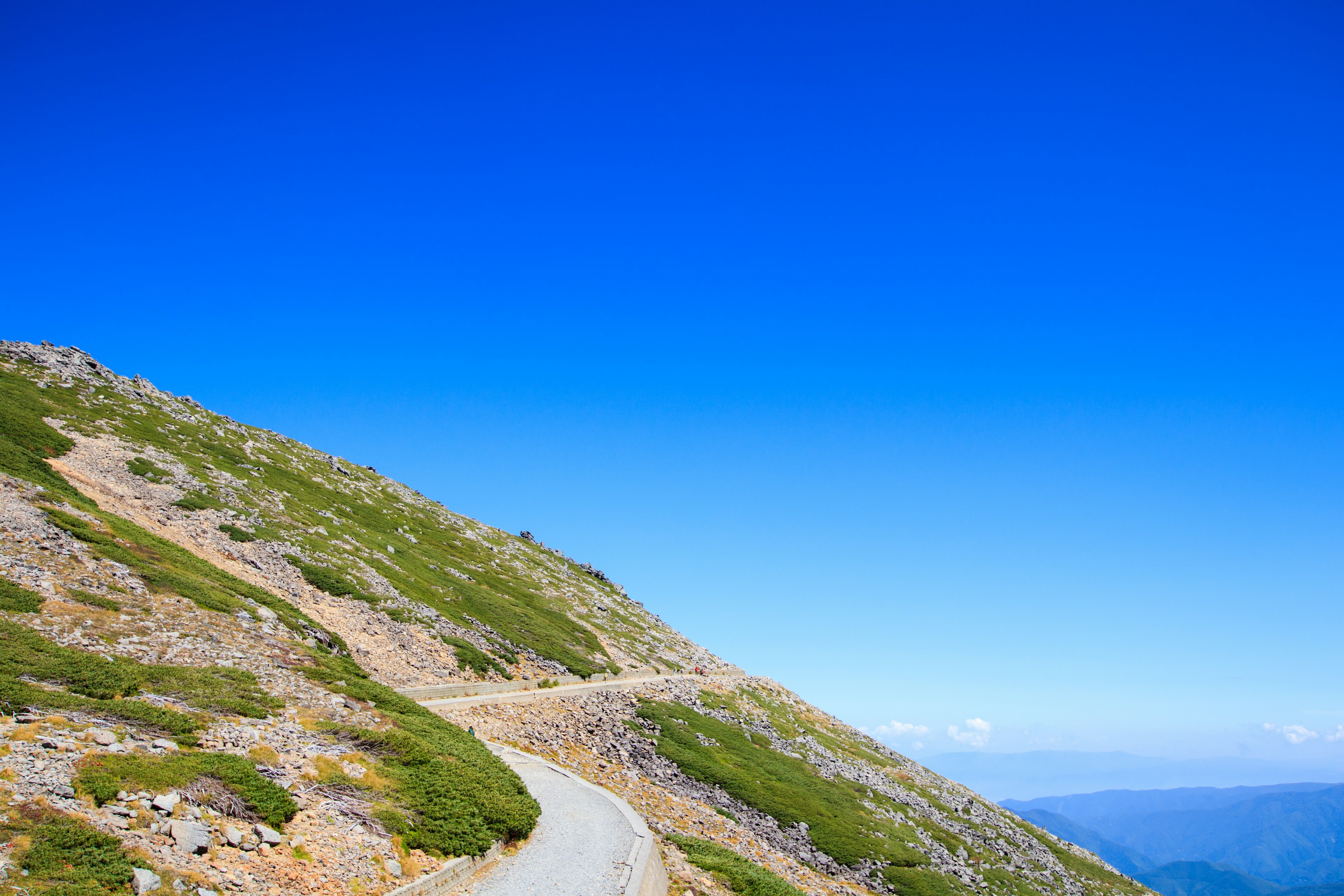 Sentiero di montagna sotto un cielo blu chiaro con vegetazione verde