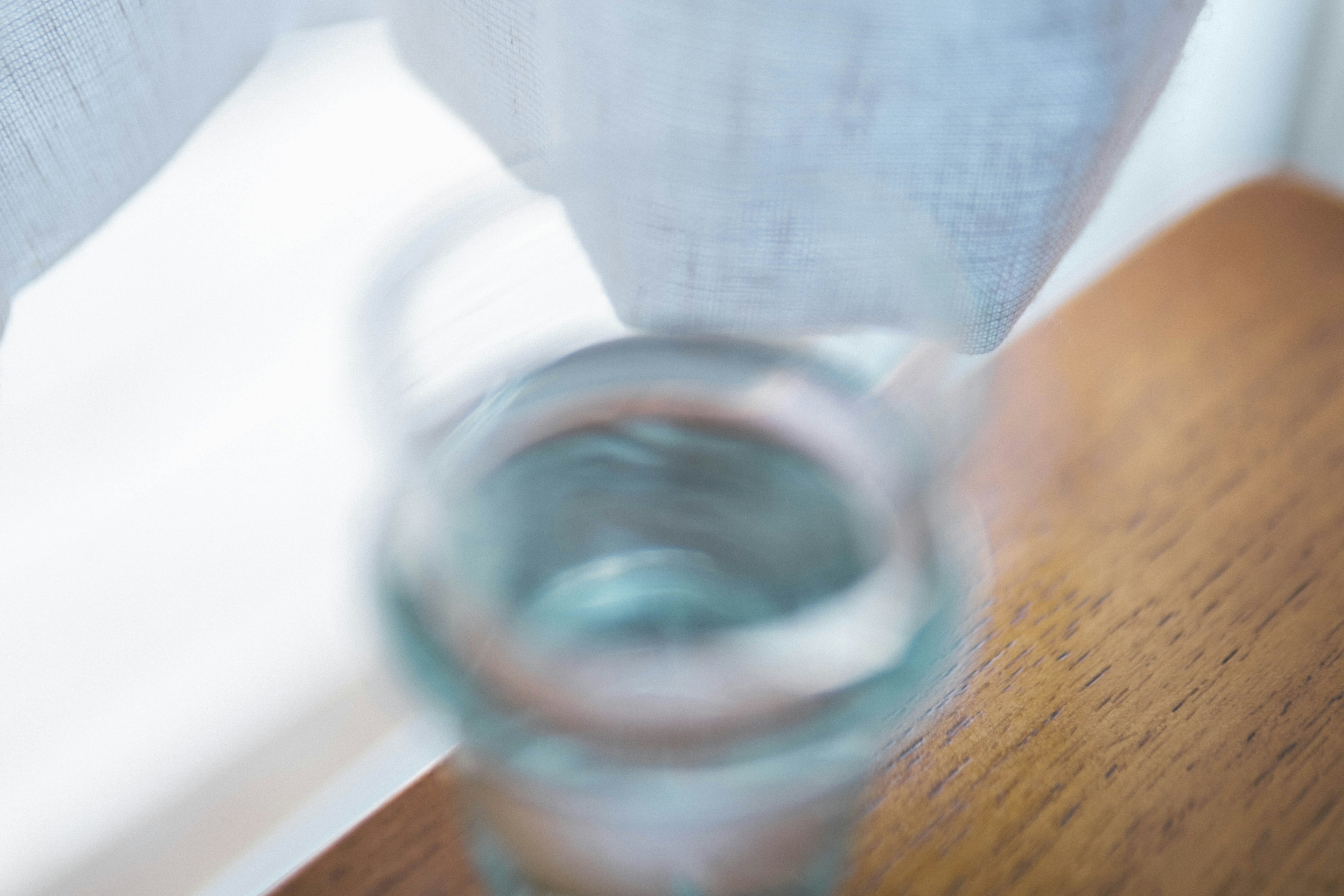 Blurred glass container with water near a white curtain