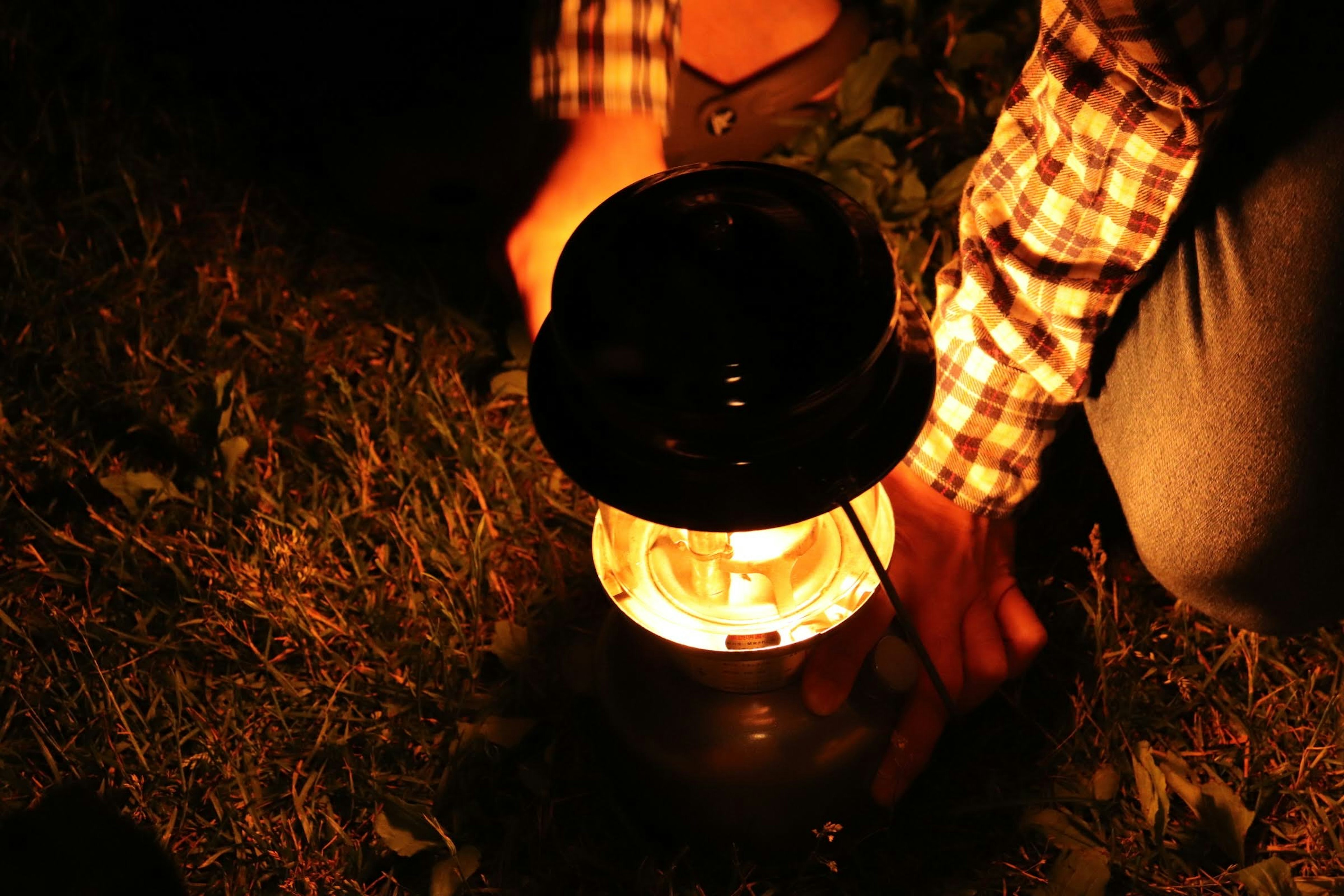 A hand lighting a lantern on the grass at night