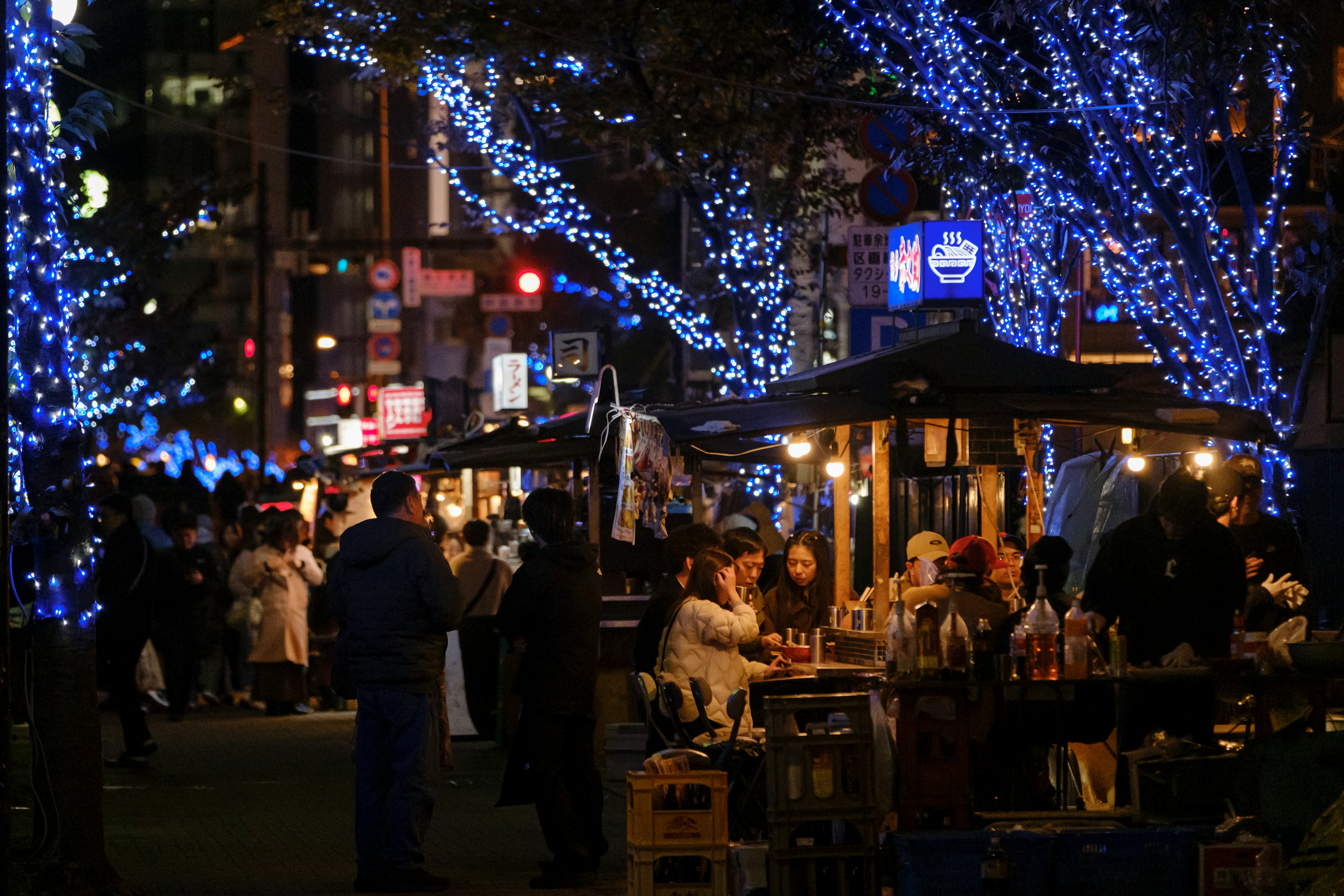 Scena notturna con luci blu vivaci che illuminano bancarelle di cibo e folle