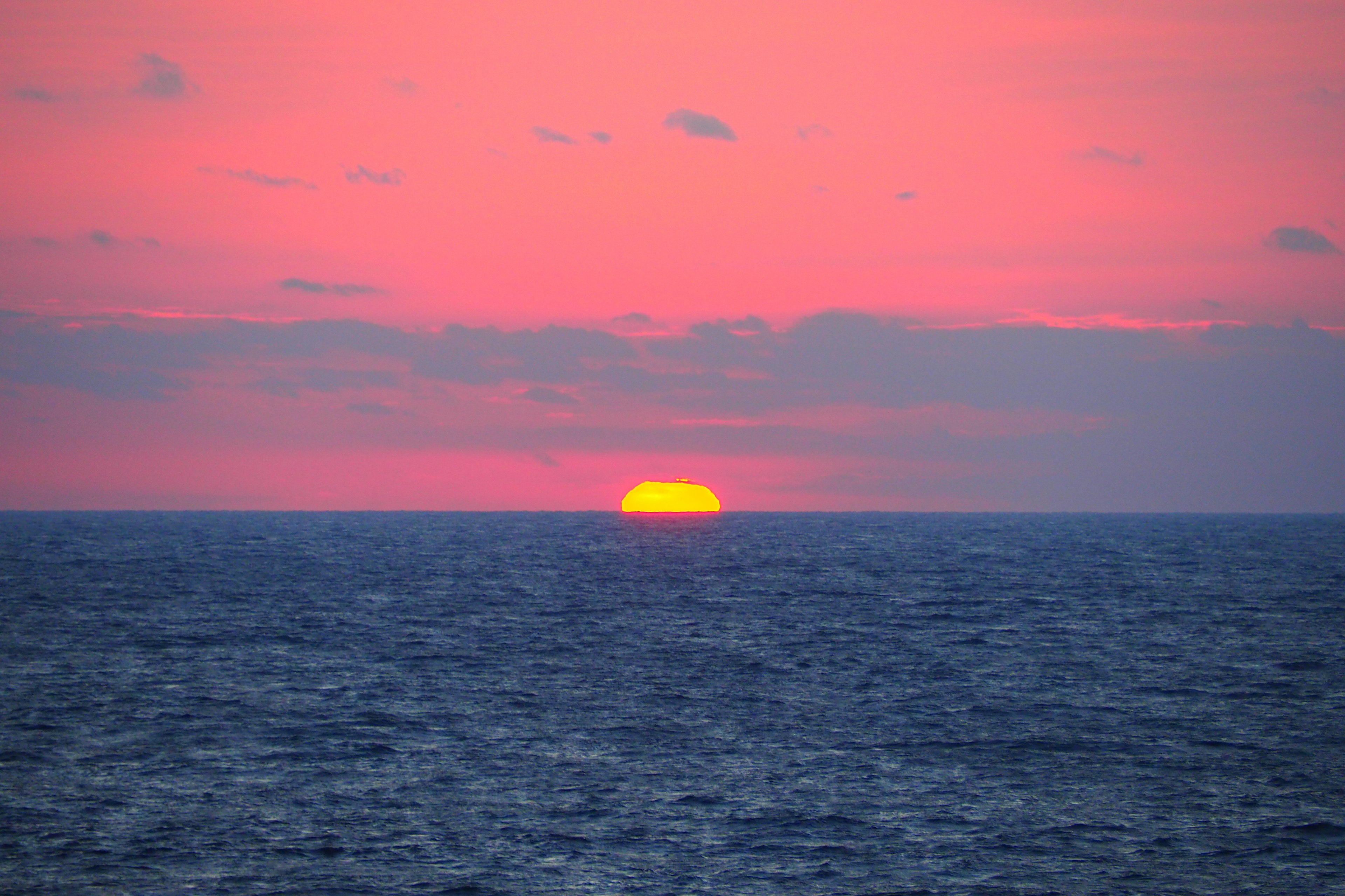 海の水平線の上に沈む夕日とピンクの空