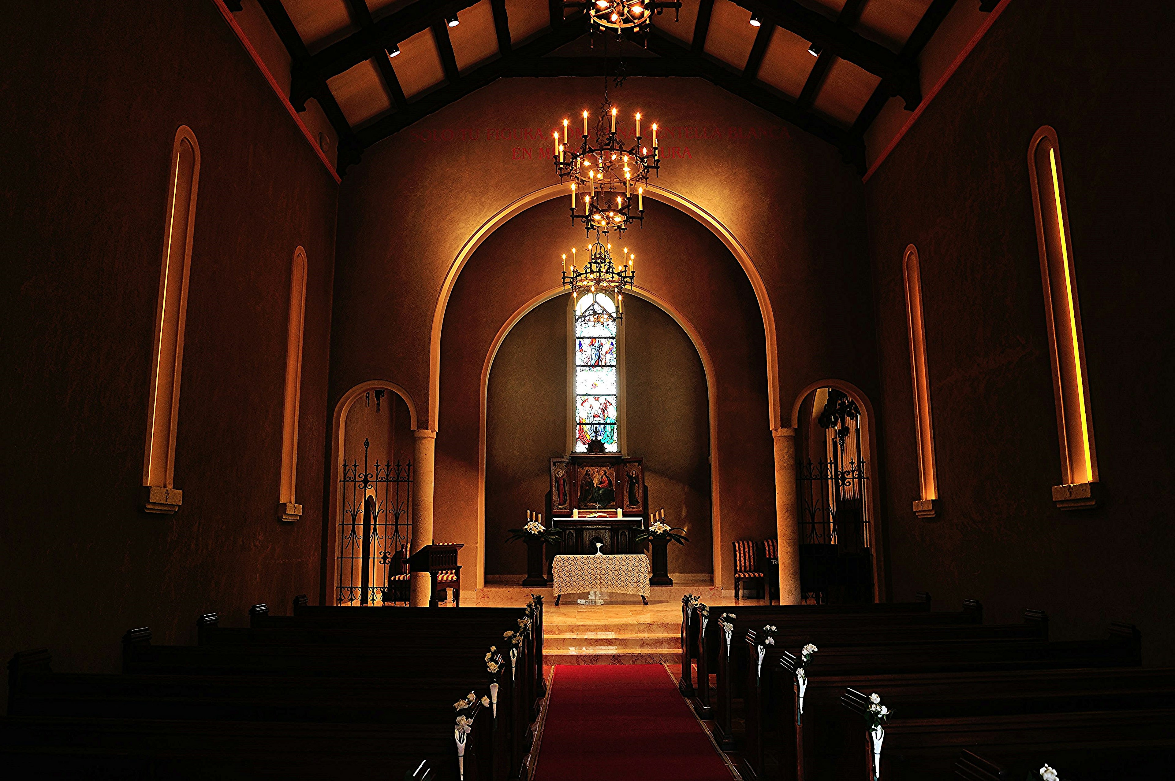 Intérieur d'une église faiblement éclairée avec un autel et des vitraux, des lustres suspendus