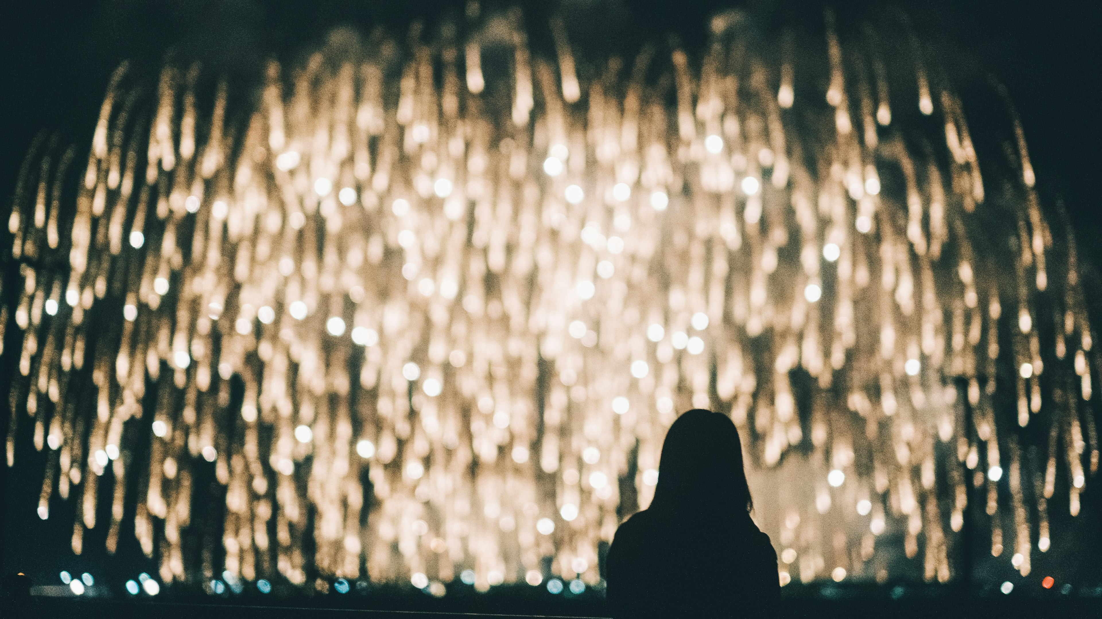 Silhouette of a person standing in front of a glowing fountain at night