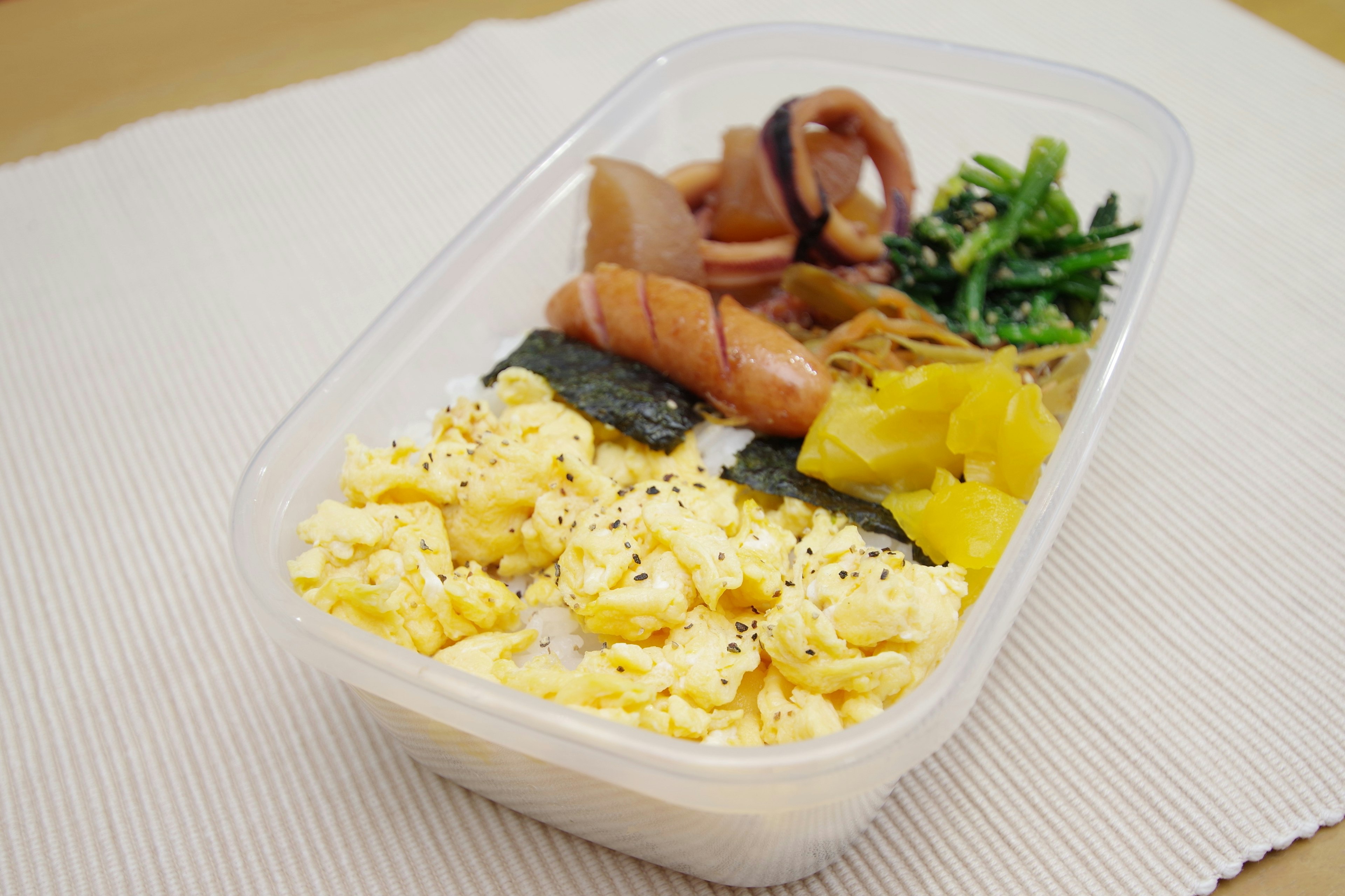 Kotak bento dengan telur orak-arik, rumput laut, sayuran, dan cumi