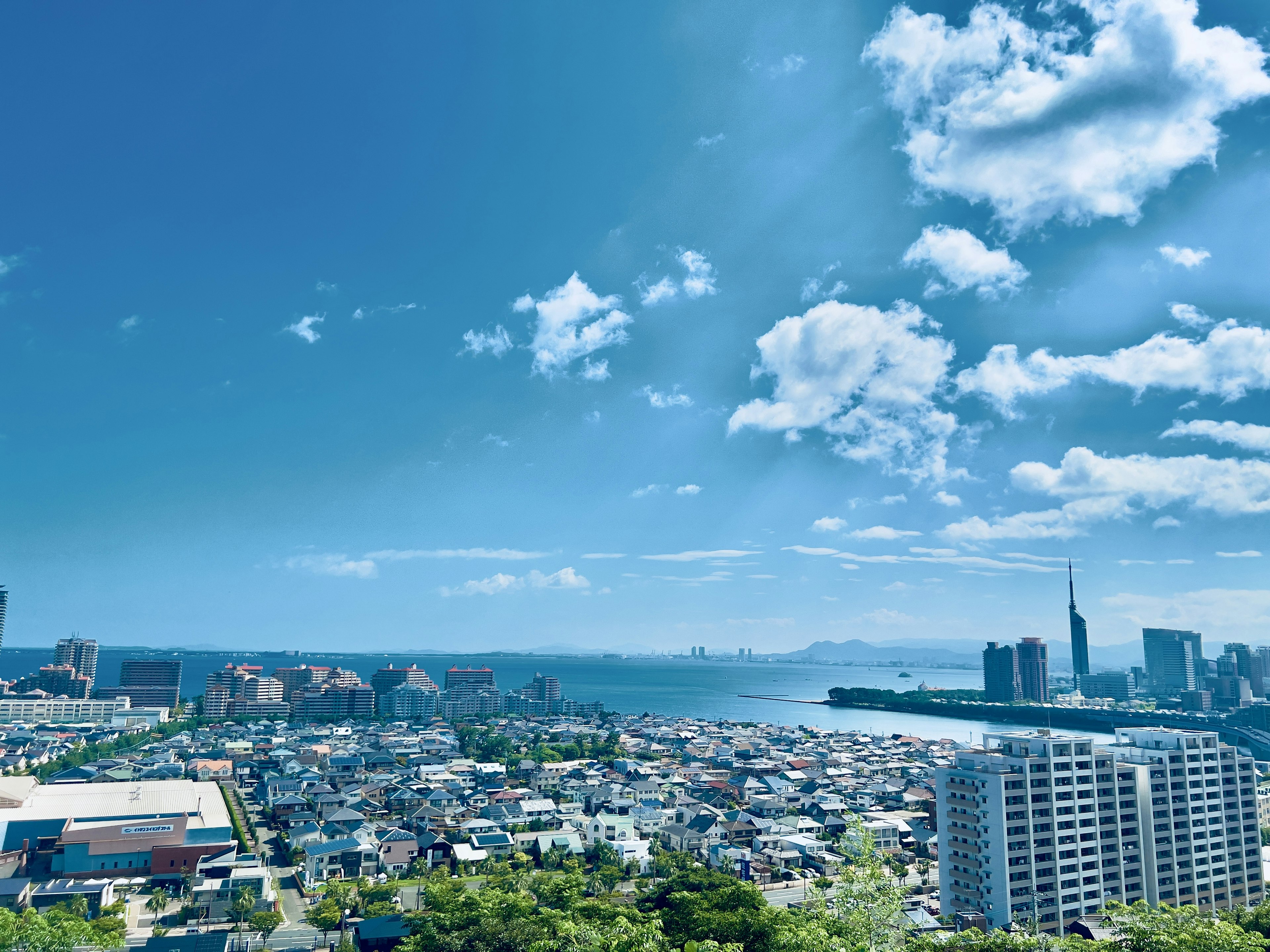 Vista panoramica di una città sotto un cielo blu con nuvole, con il mare e grattacieli