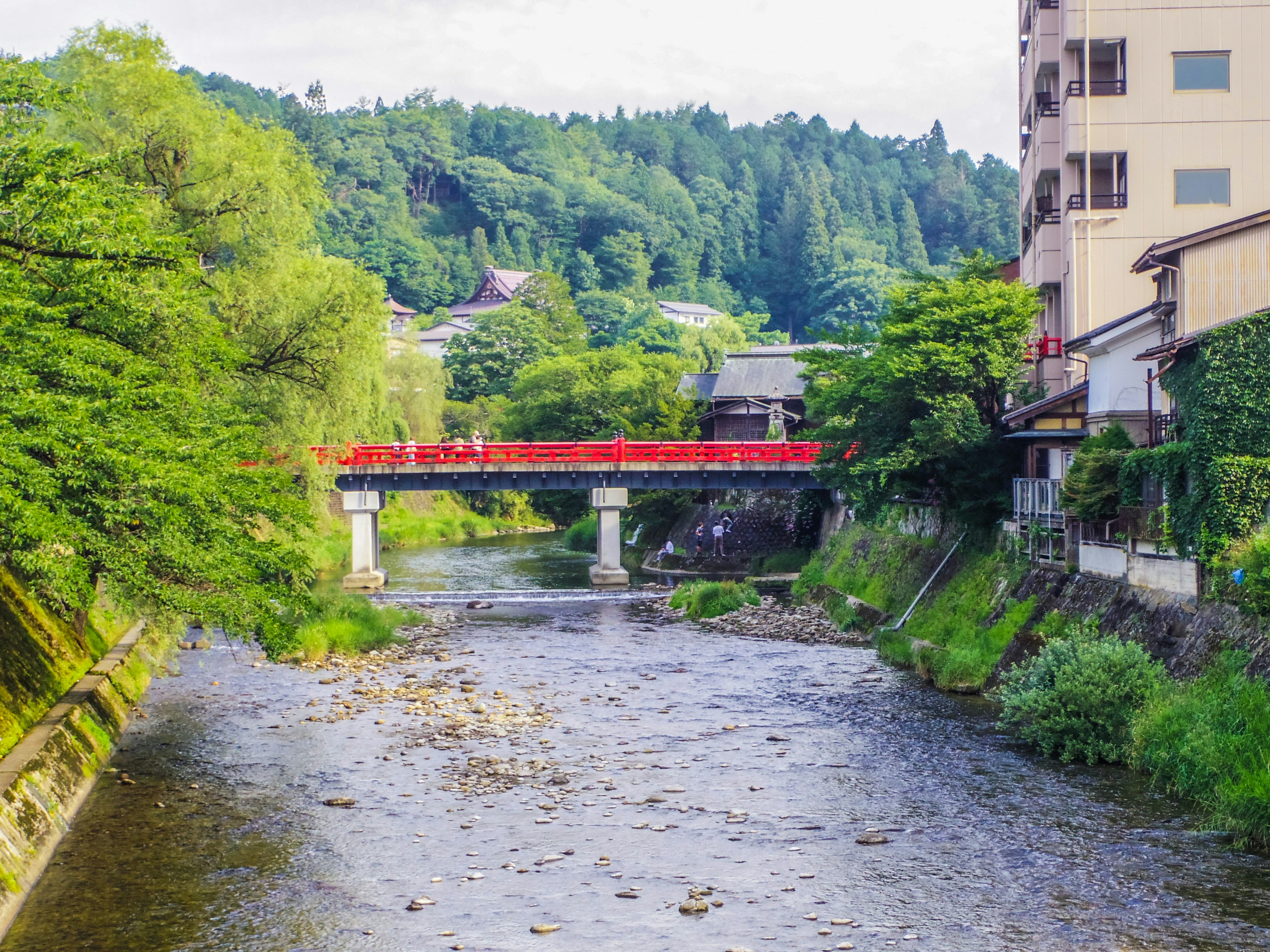 Malersicher Blick auf einen Fluss mit einer roten Brücke und üppigen grünen Bergen