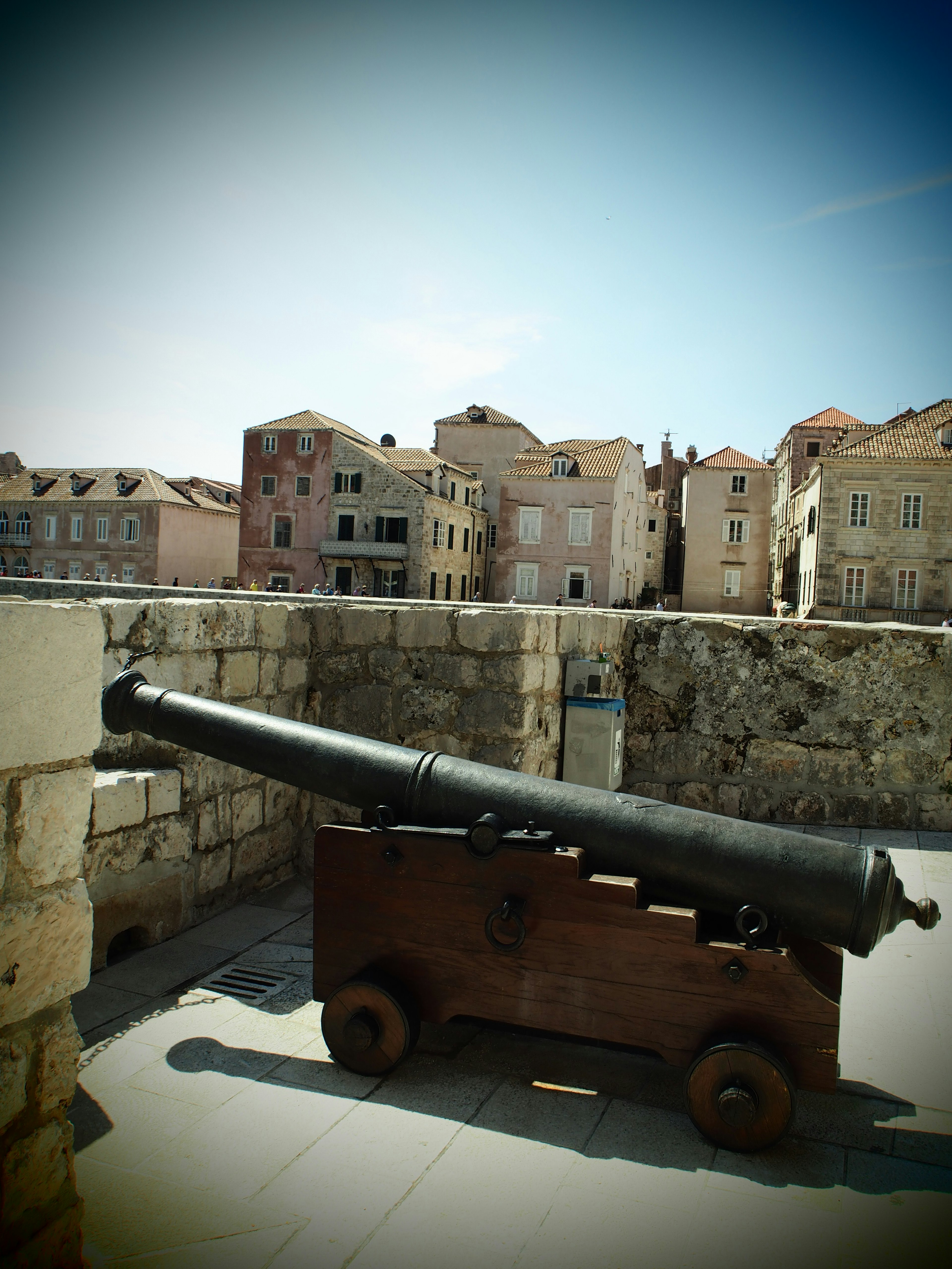 An old cannon positioned near a stone wall with historic buildings in the background