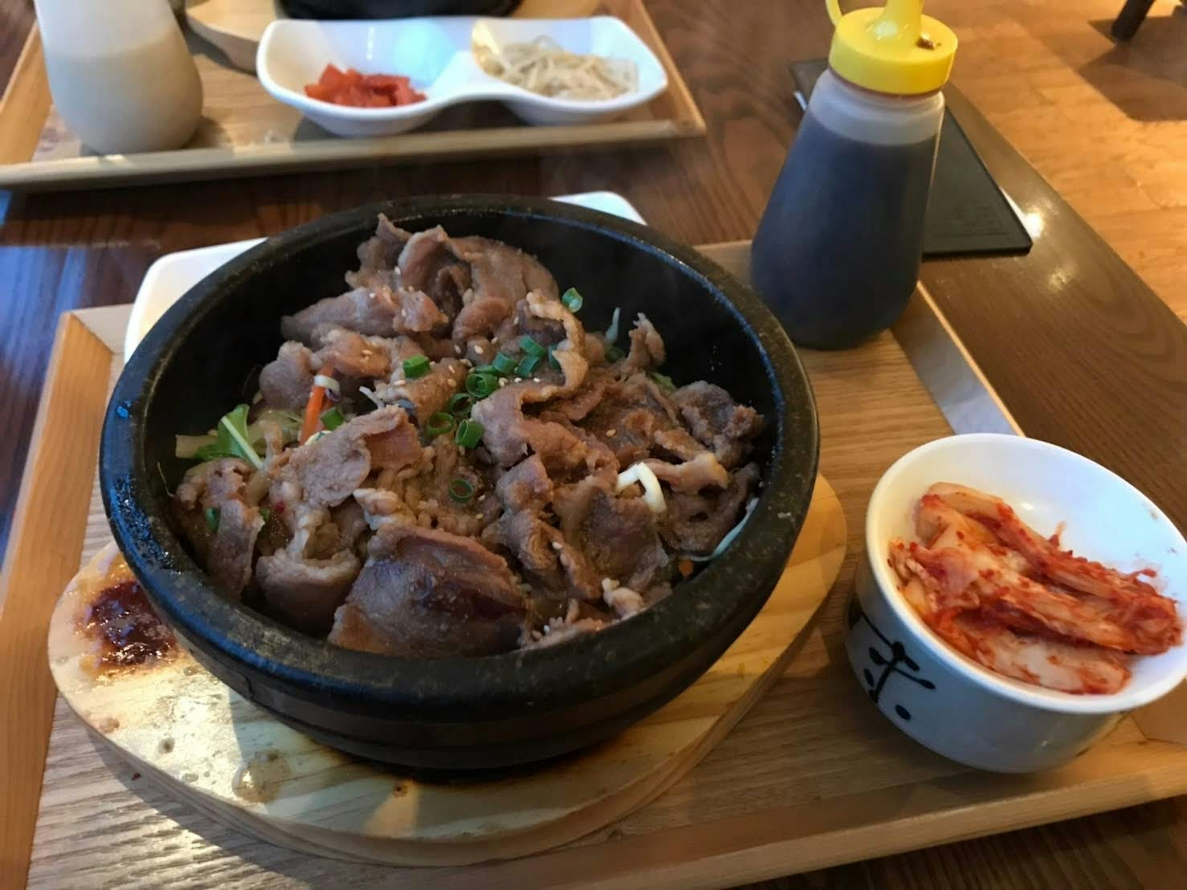 Tazón de piedra caliente lleno de plato de carne y guarnición de kimchi