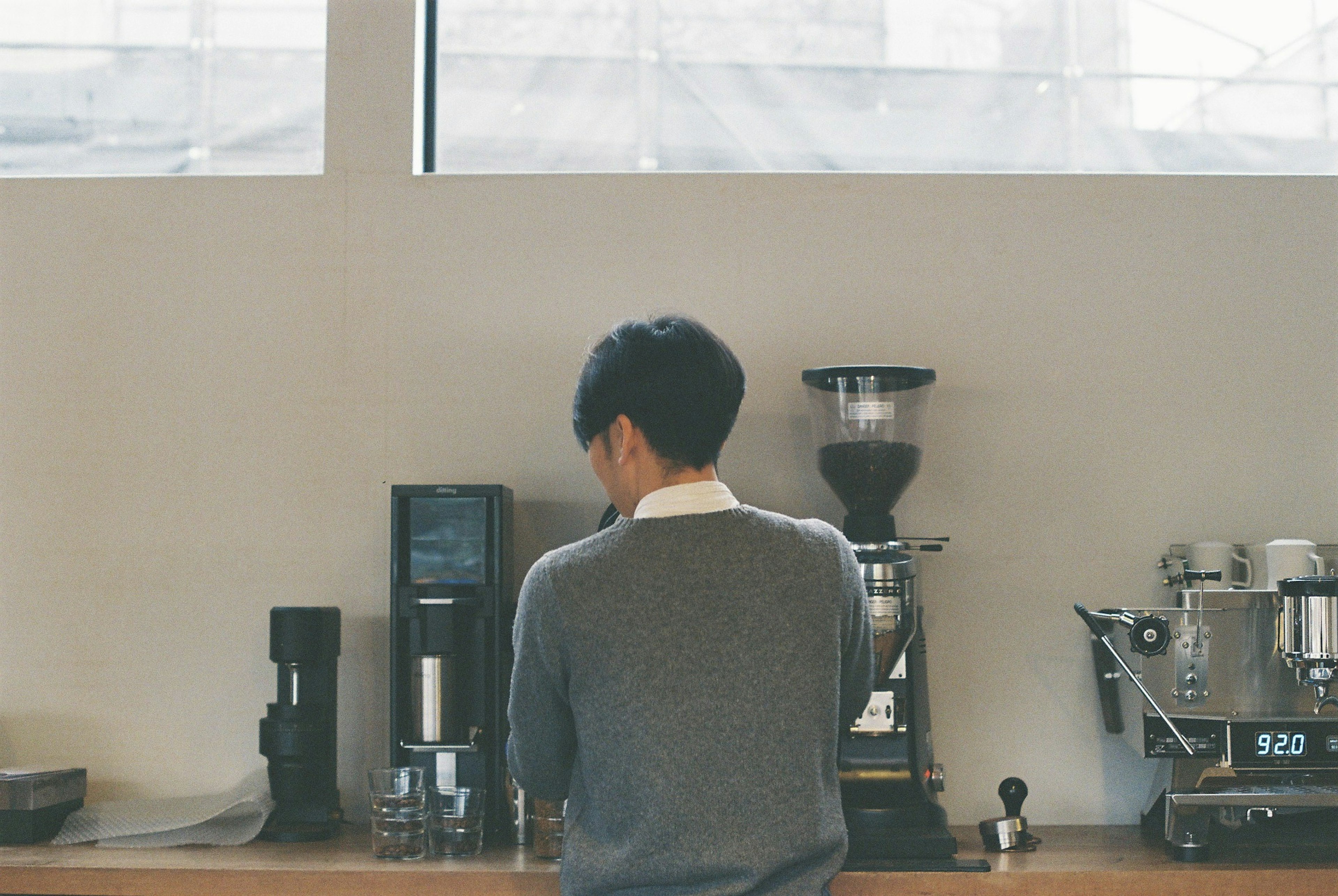 Ein Mann, der in einem Café Kaffee zubereitet, von hinten mit Kaffeegeräten gesehen