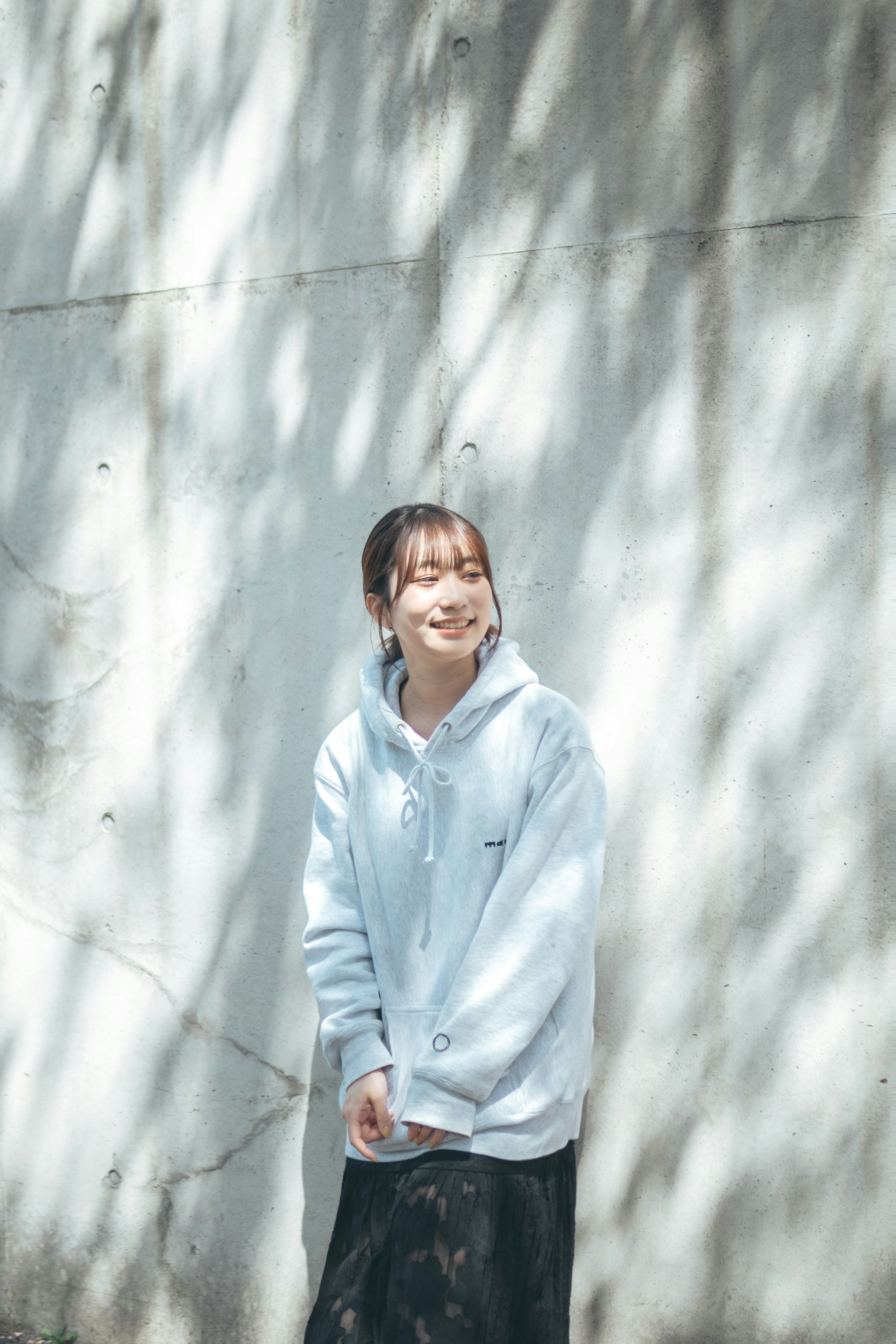 Một người phụ nữ trong áo hoodie màu xanh đang cười đứng trước một bức tường bê tông