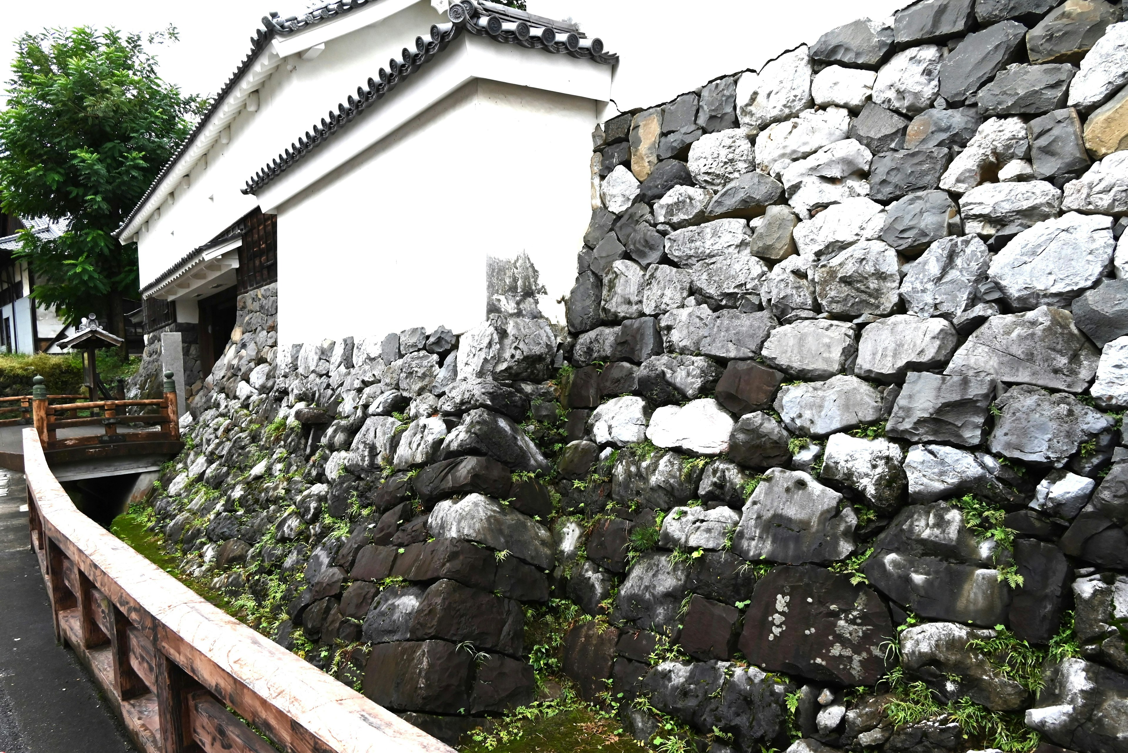 Muro de piedra con edificio blanco y vegetación al fondo