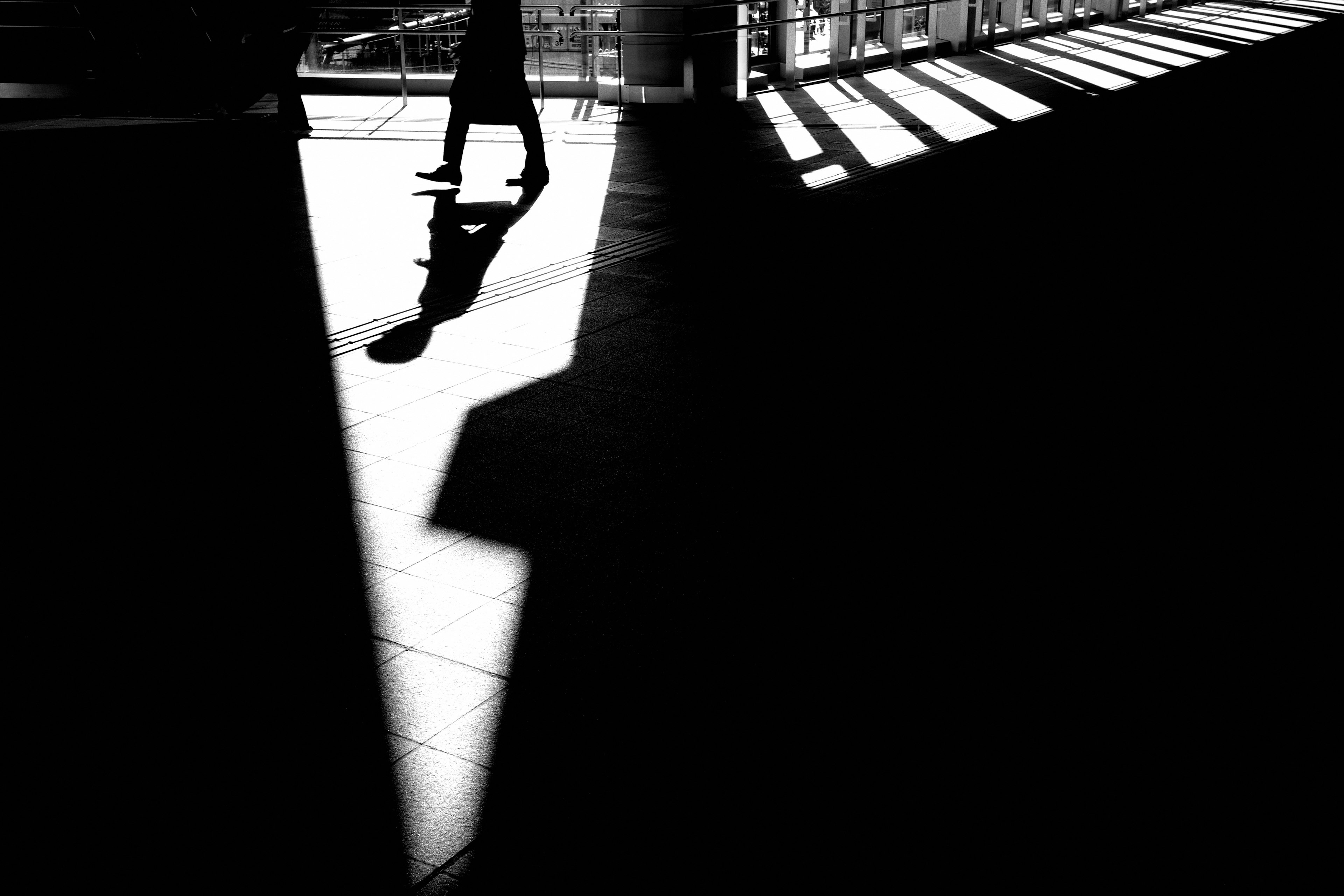Image en noir et blanc mettant en avant un fort contraste entre lumière et ombre une personne marchant est visible