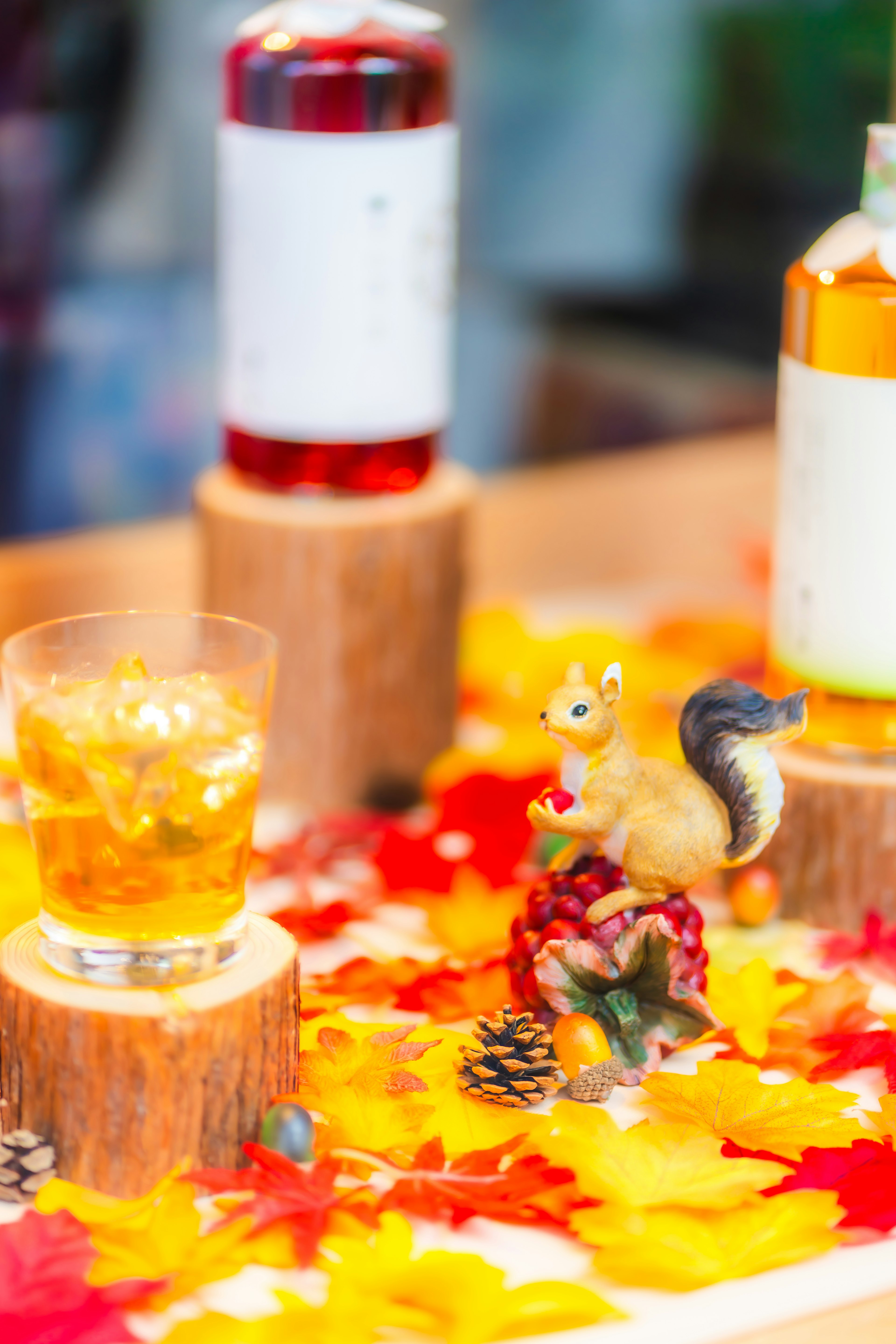 Mesa decorada con hojas de otoño coloridas que presenta botellas de bebida y una figura de ardilla