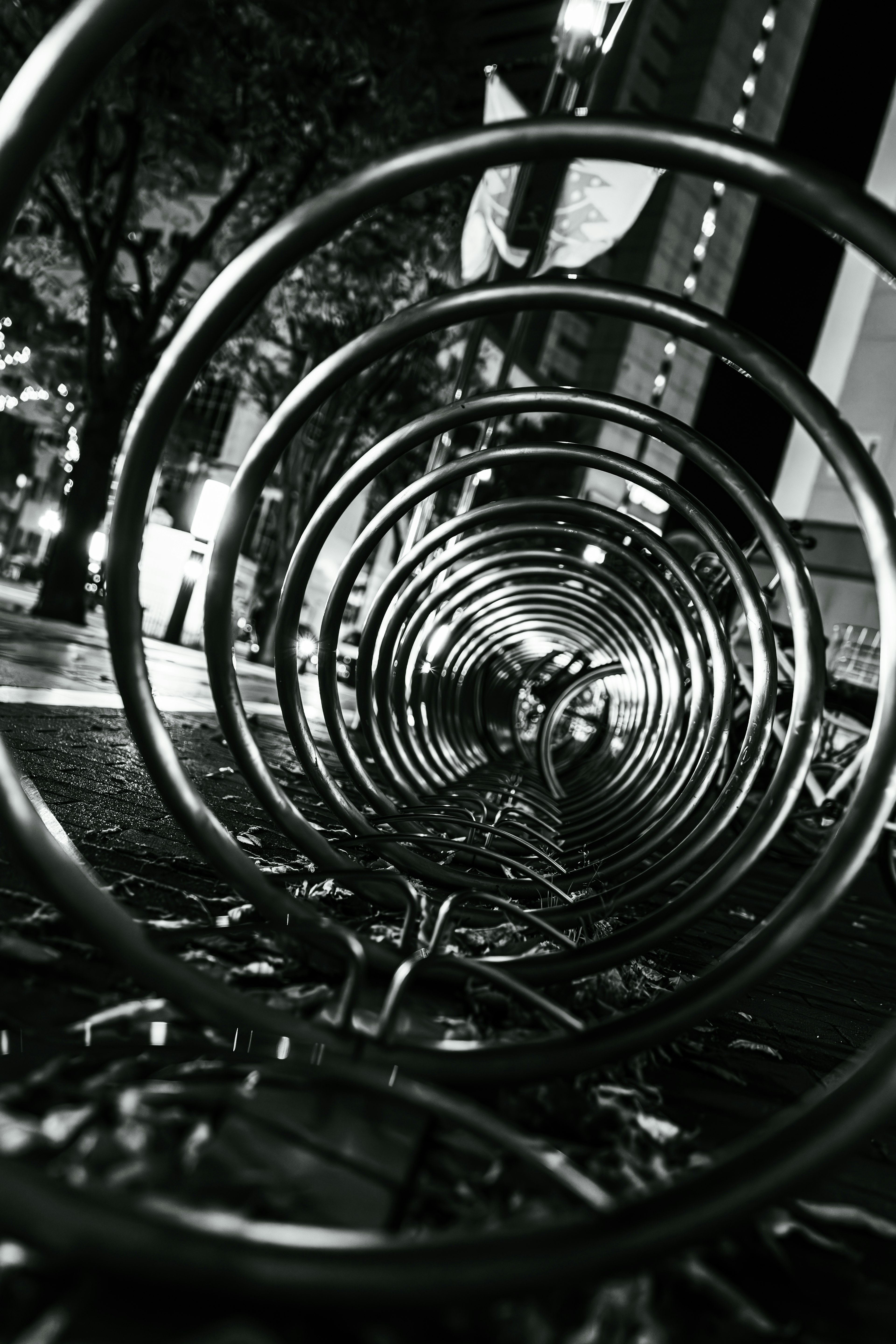 Black and white image of a bicycle rack in an urban setting Spiral design with surrounding trees