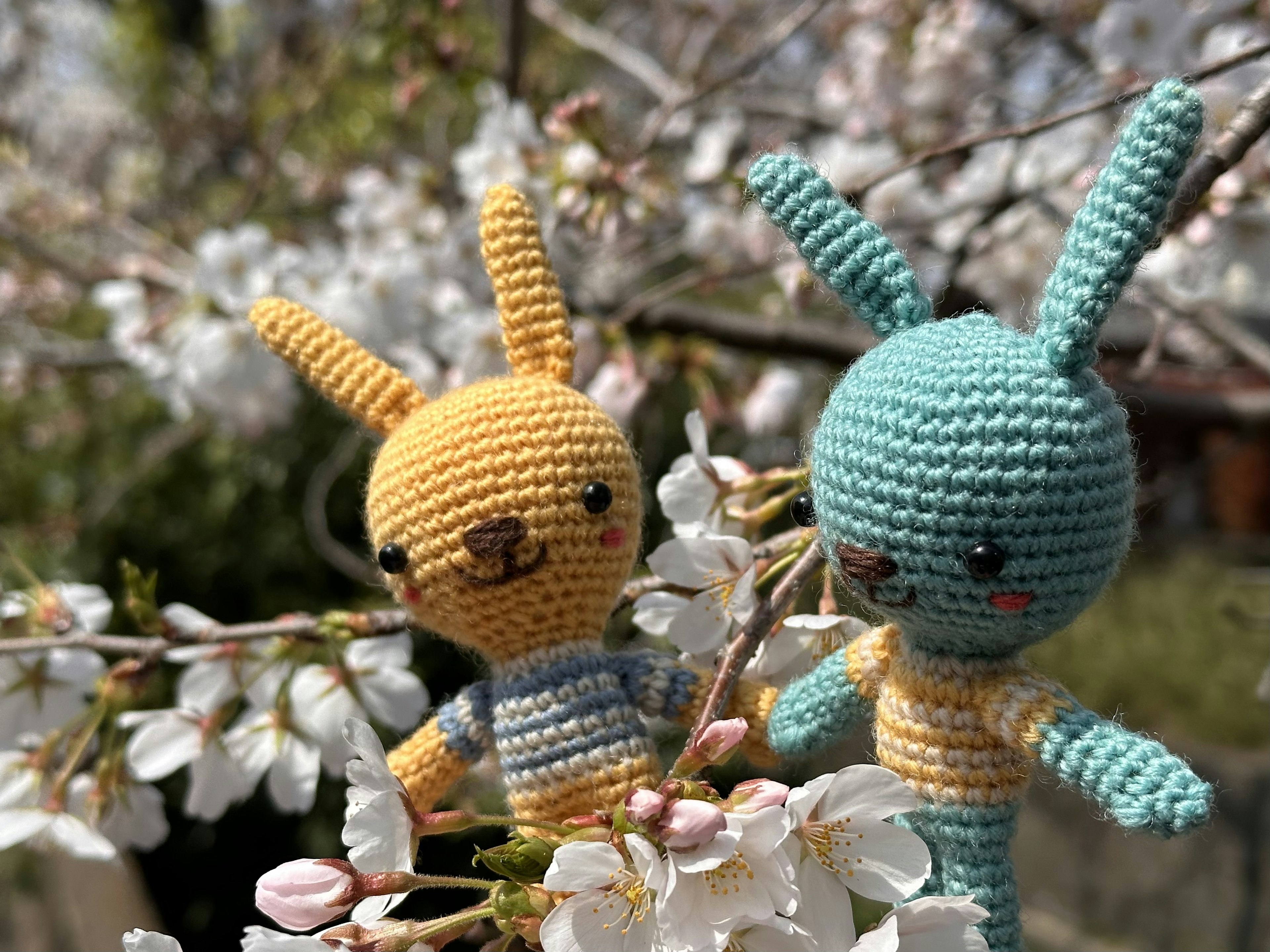 Deux jouets en crochet colorés en forme de lapin parmi des cerisiers en fleurs