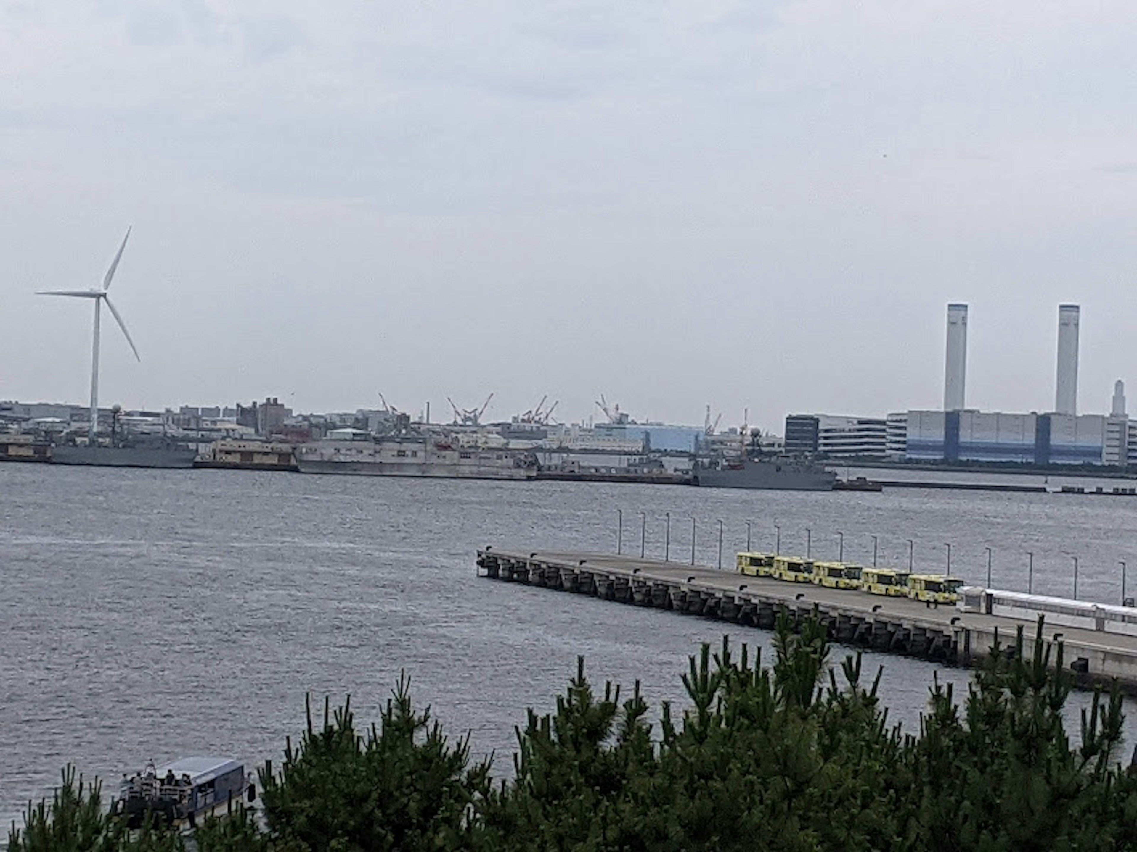 Landschaft von Meer und Industriegebiet mit einem Windrad und Schornsteinen