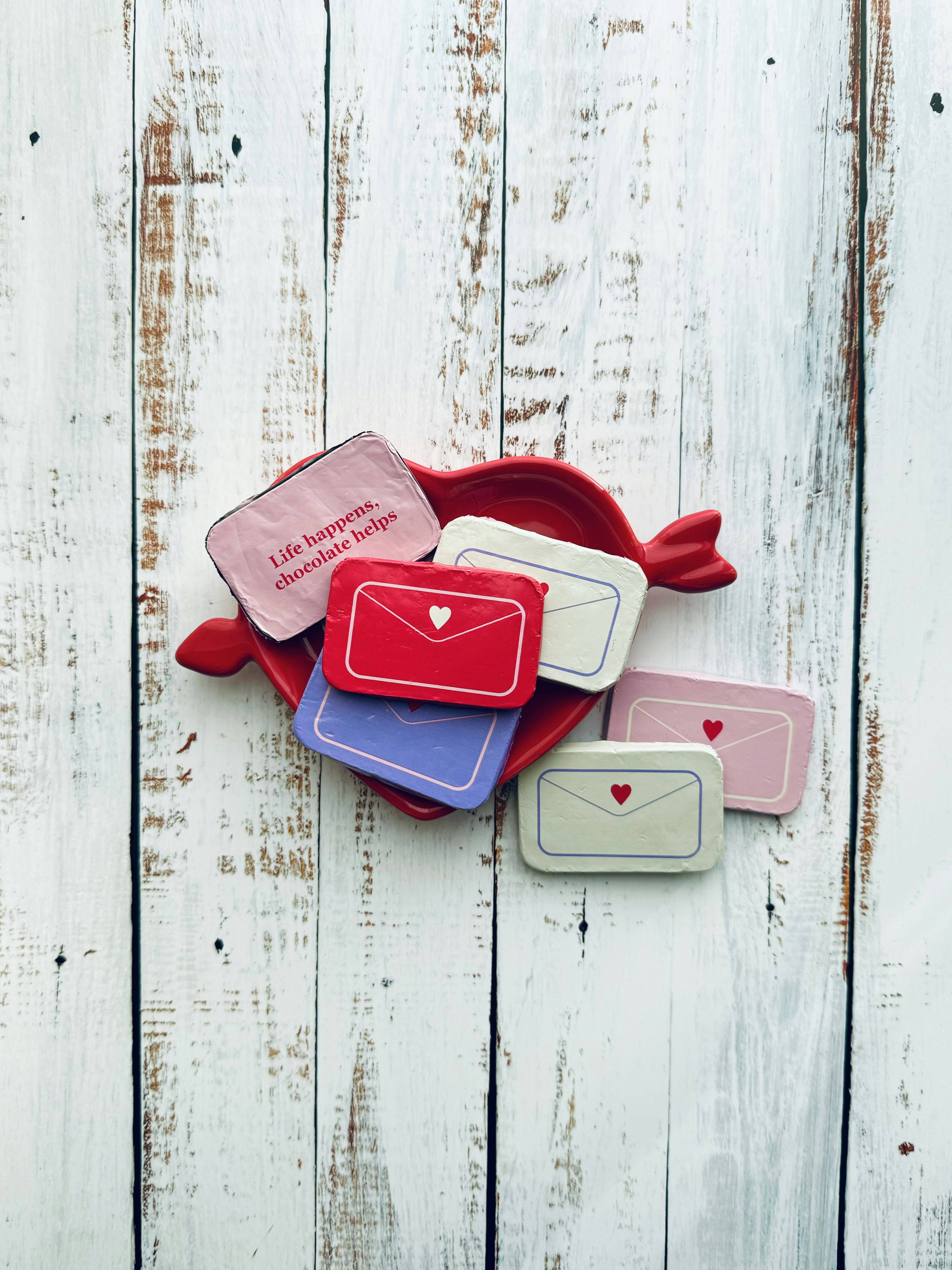 Galletas en forma de sobre de colores dispuestas sobre un cojín rojo con forma de corazón