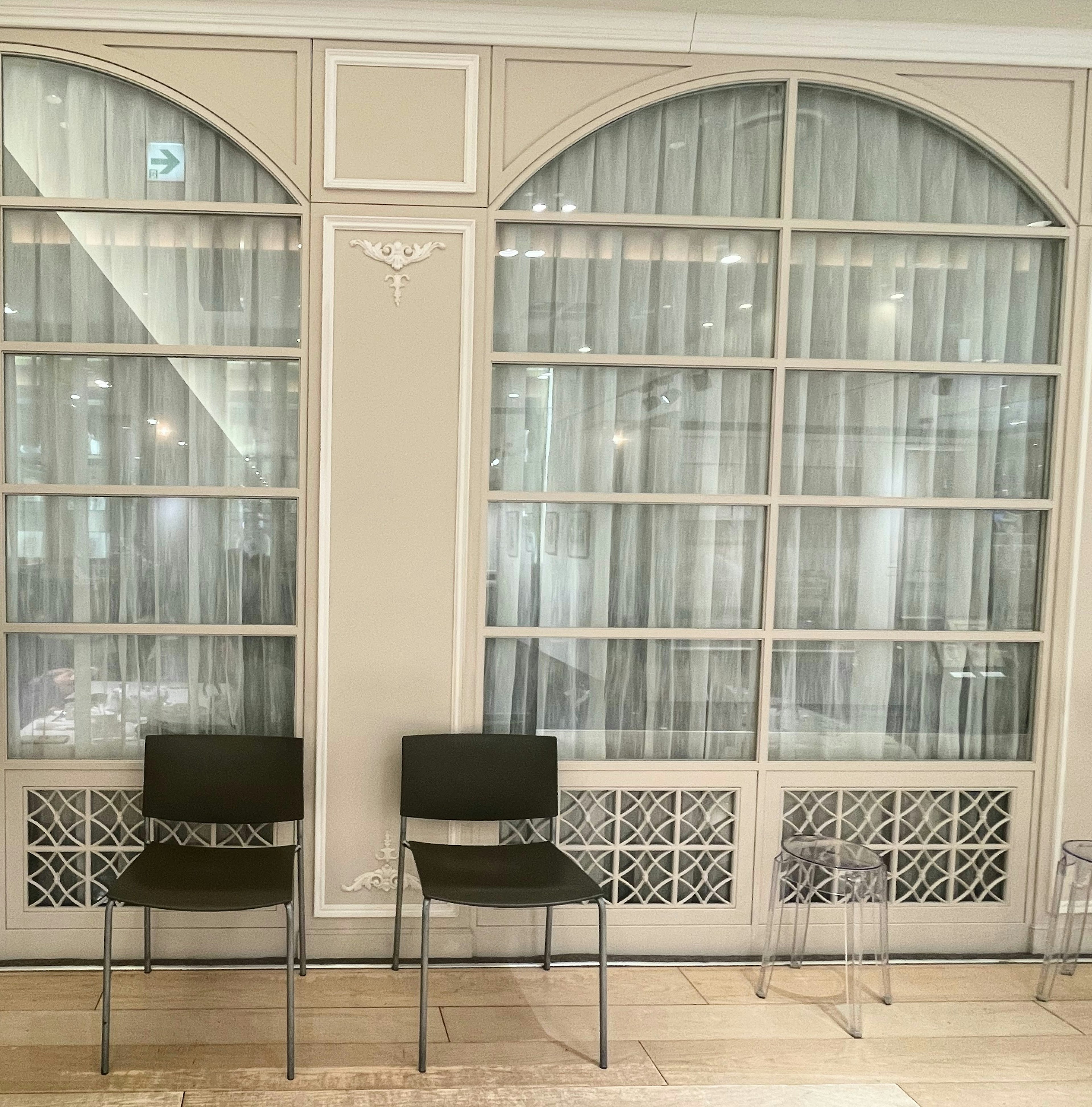 Black chairs and transparent chairs in front of arched windows with white curtains