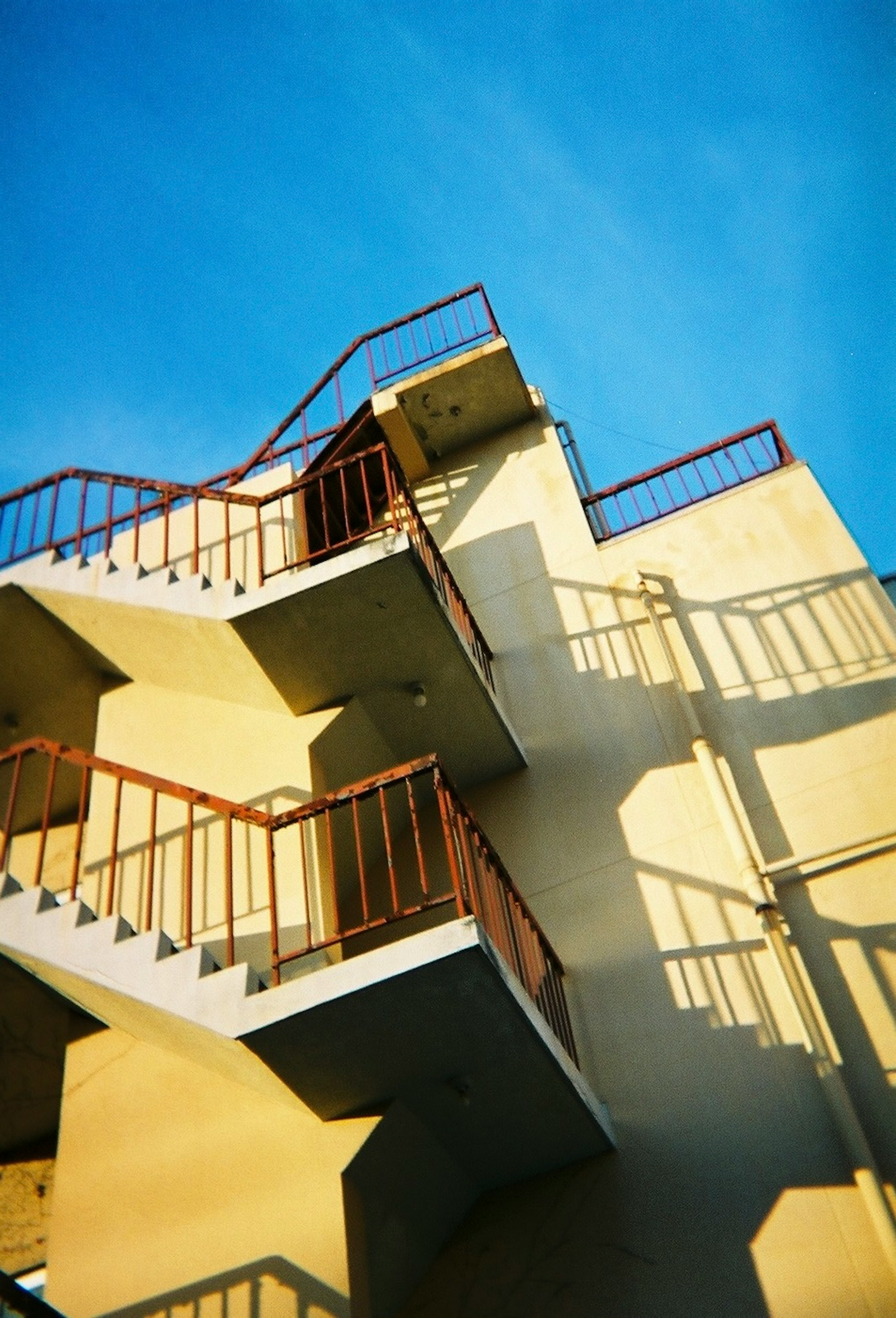 Vista esterna di un edificio con scale che proiettano ombre sotto un cielo blu