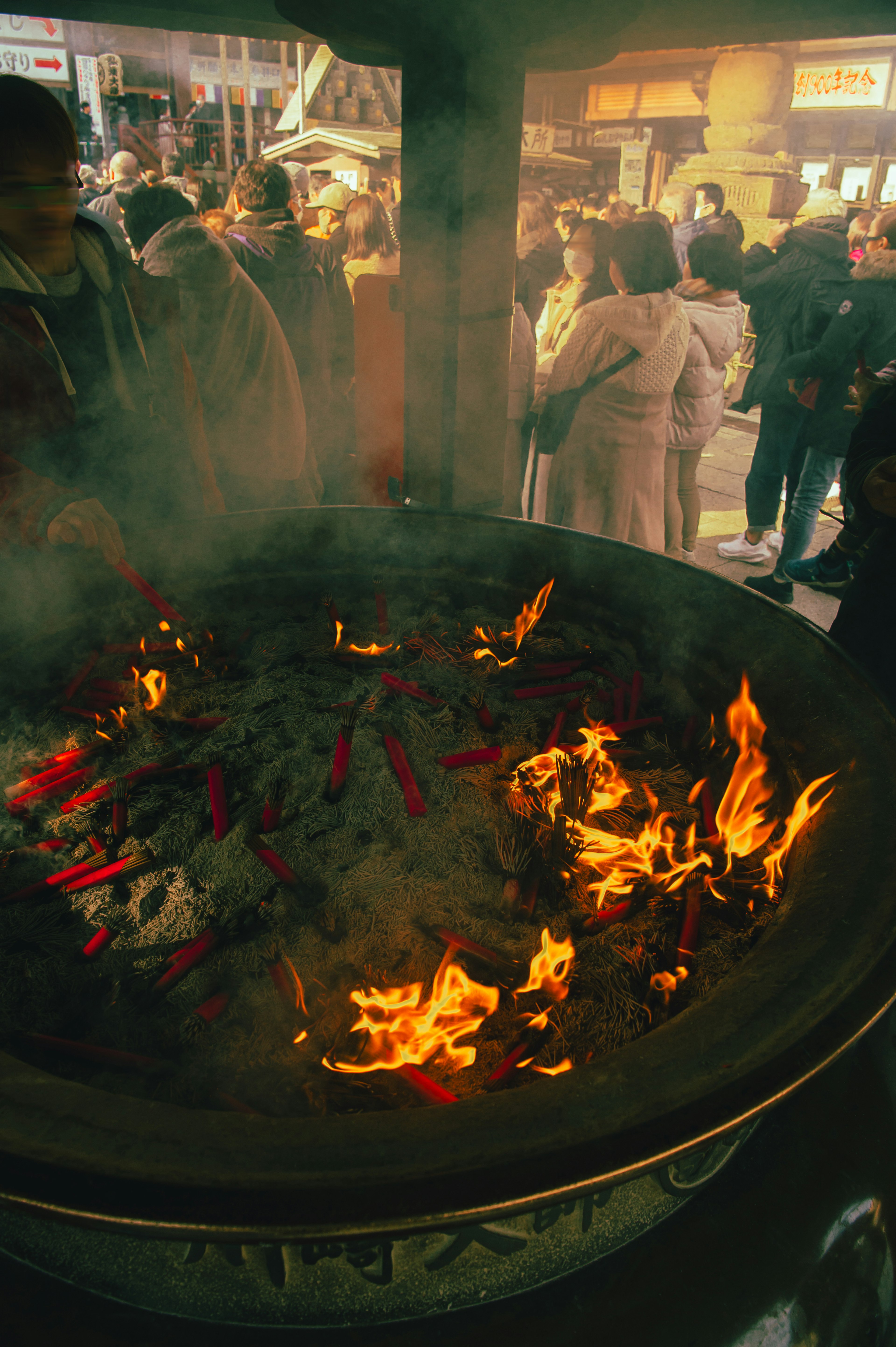 Large fire pit with flames and smoke surrounded by people