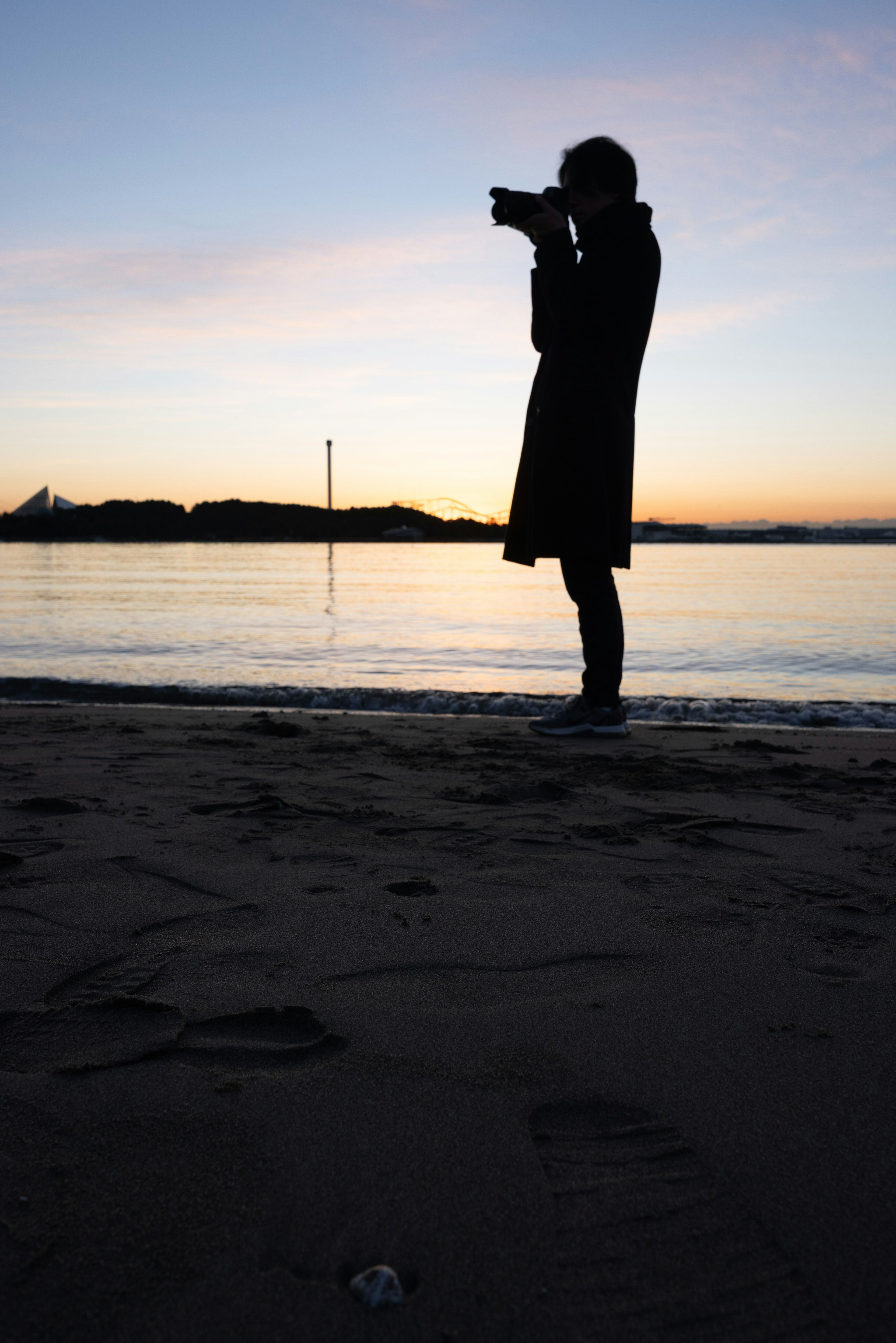 夕暮れ時に海辺でカメラを構える人物のシルエット