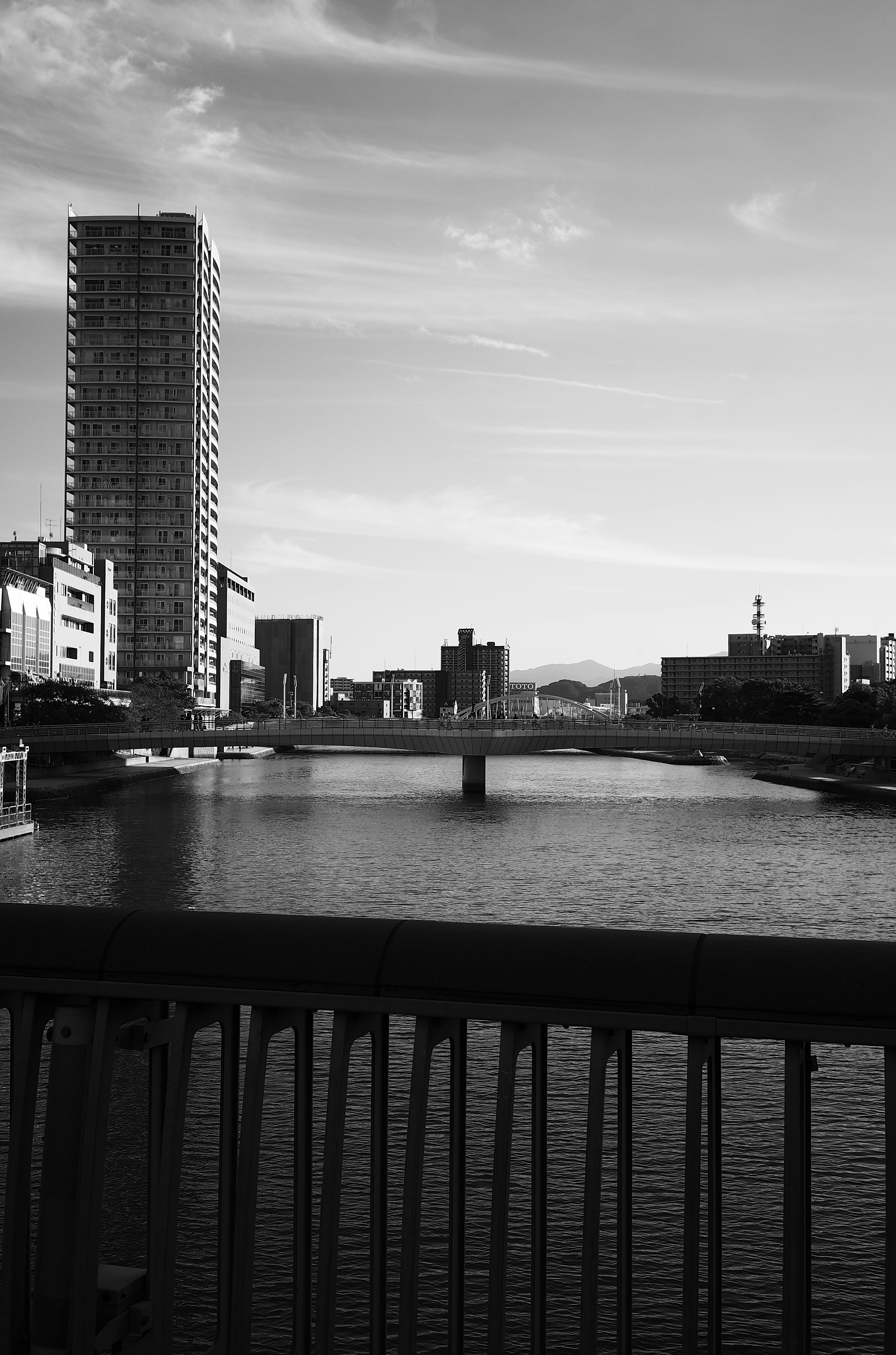 Black and white urban landscape featuring a river and bridge with tall buildings and sky