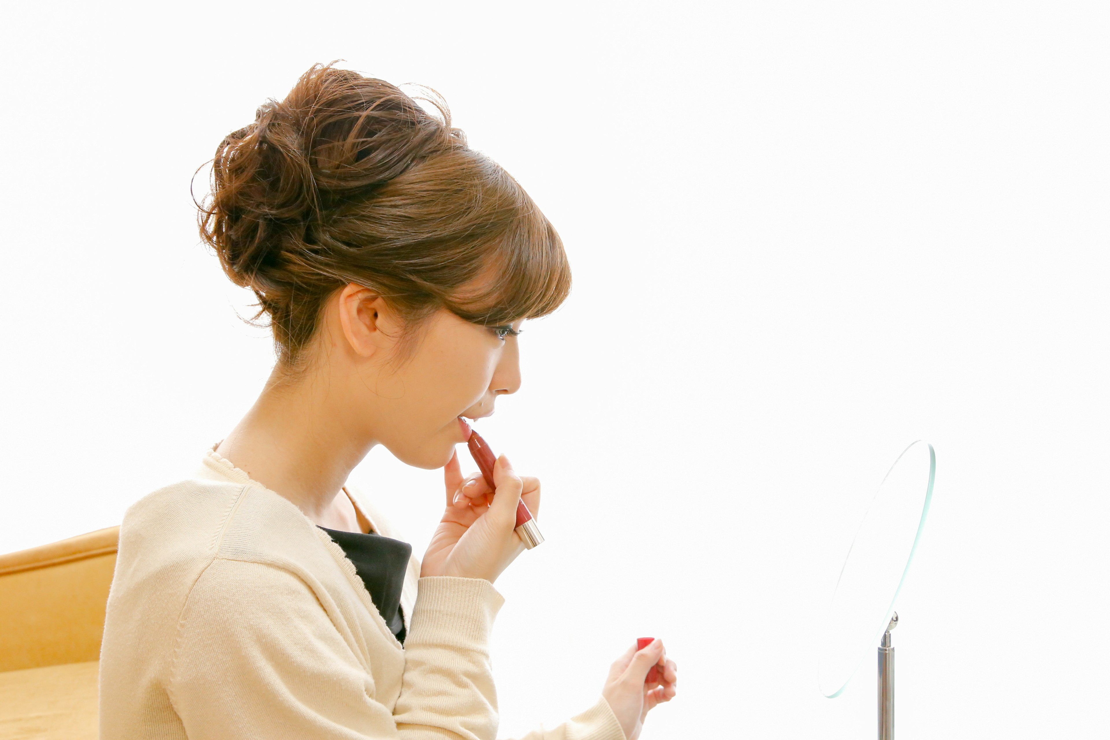 Profil d'une femme appliquant du rouge à lèvres devant un miroir coiffure douce et fond lumineux