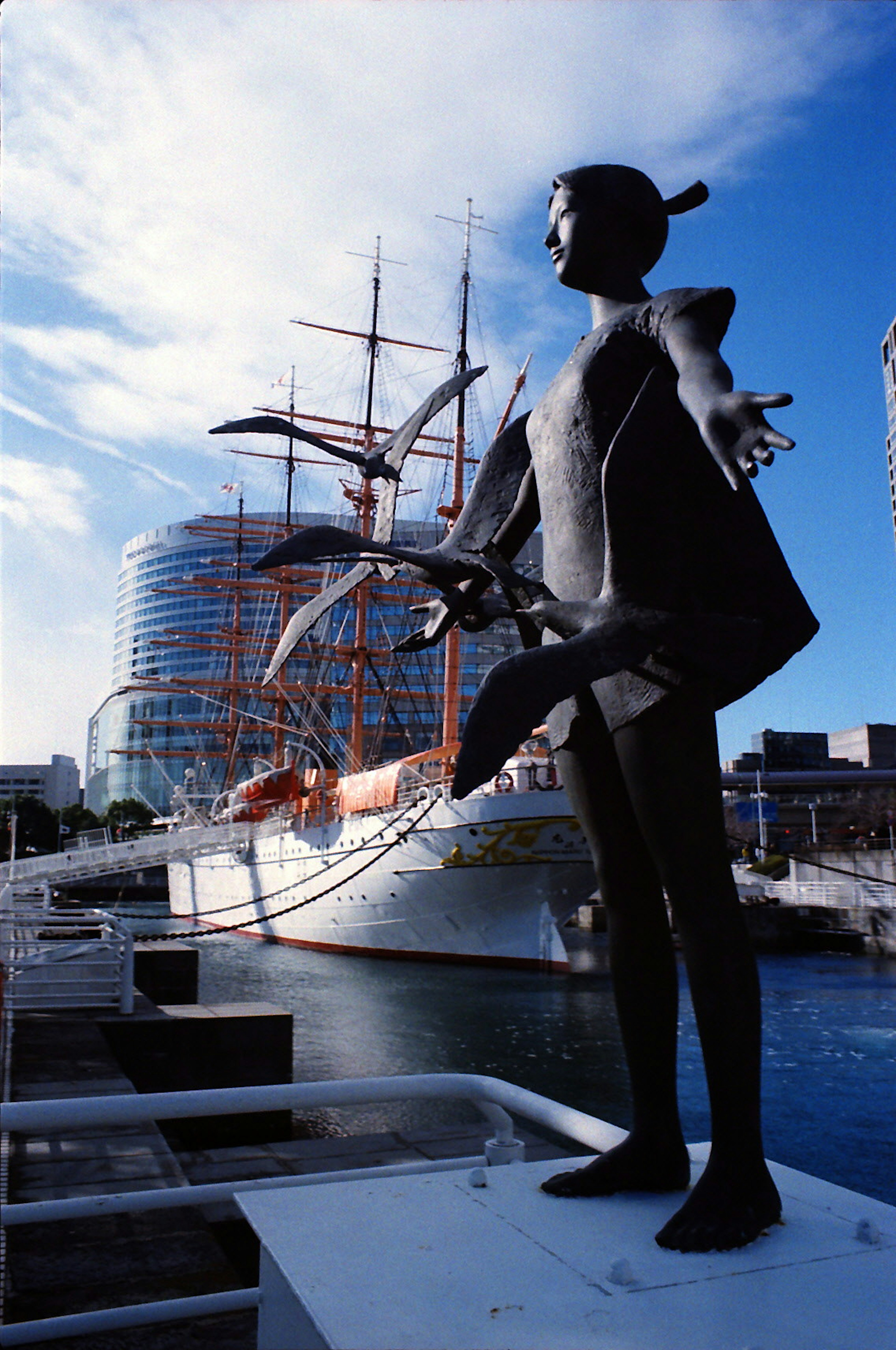 Schwarze Statue steht im Hafen mit einem Segelschiff im Hintergrund