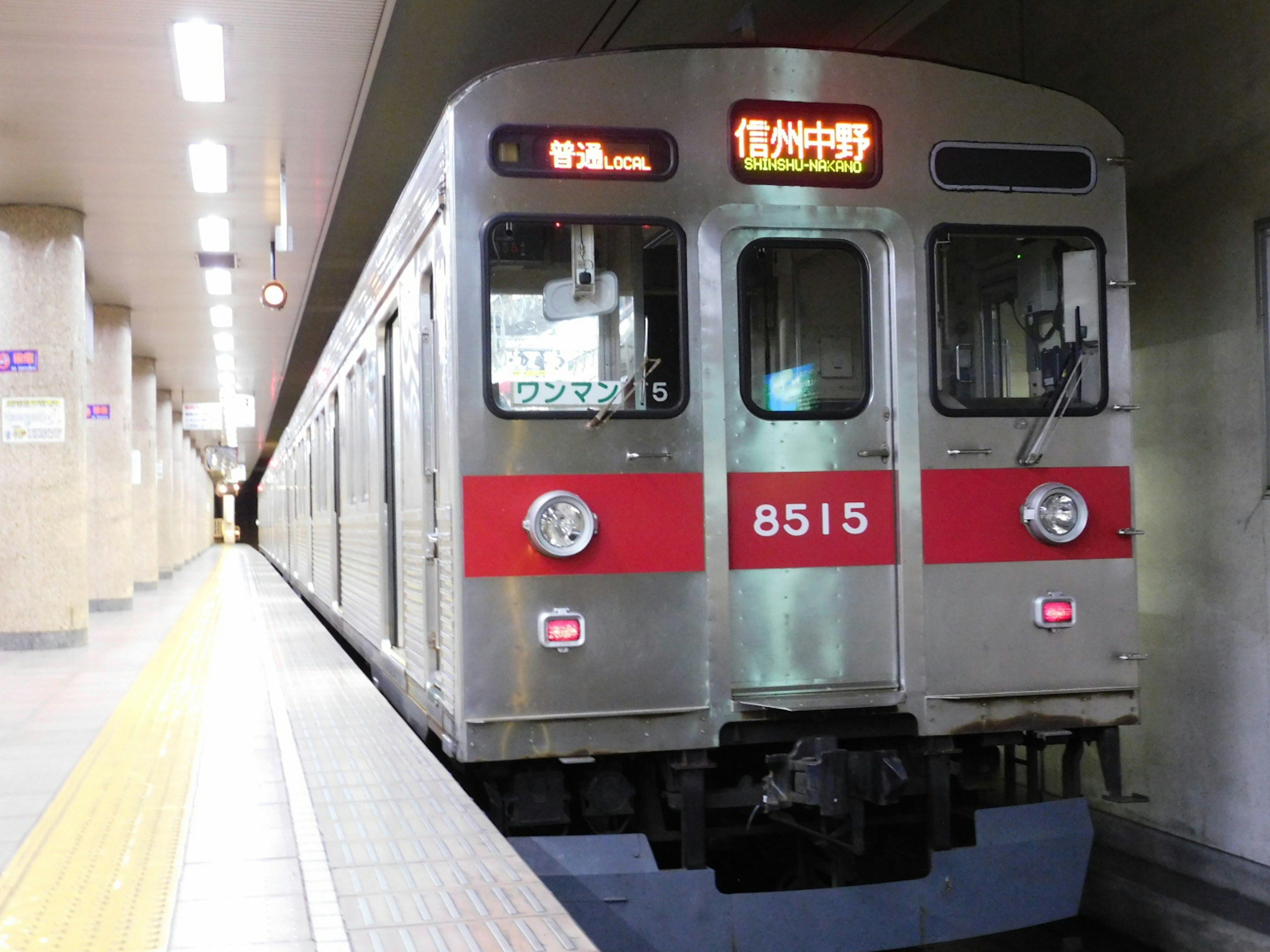 Silver train with red stripes stopped at a subway station