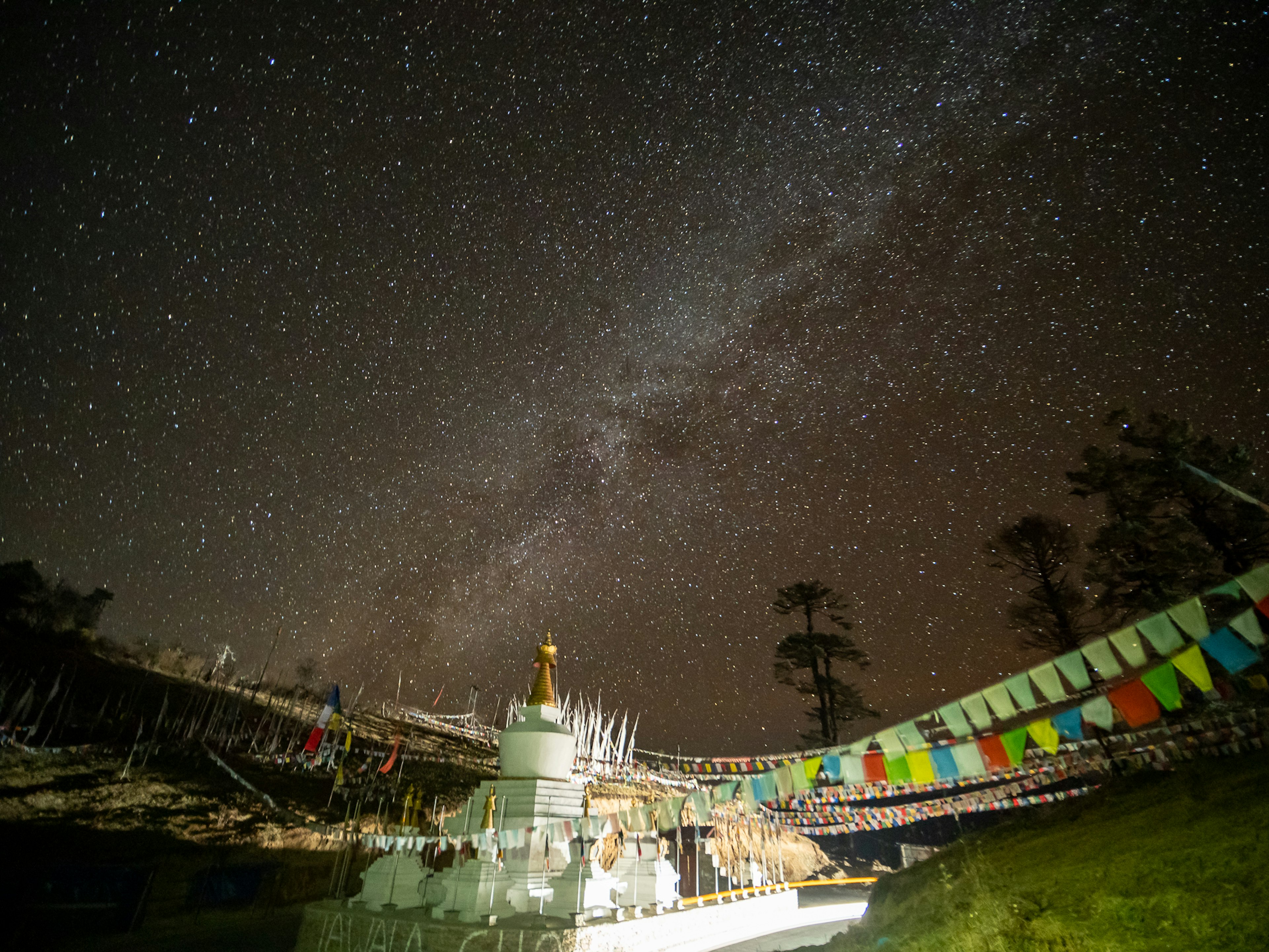 Vista escénica de una estupa bajo un cielo estrellado con banderas de oración coloridas