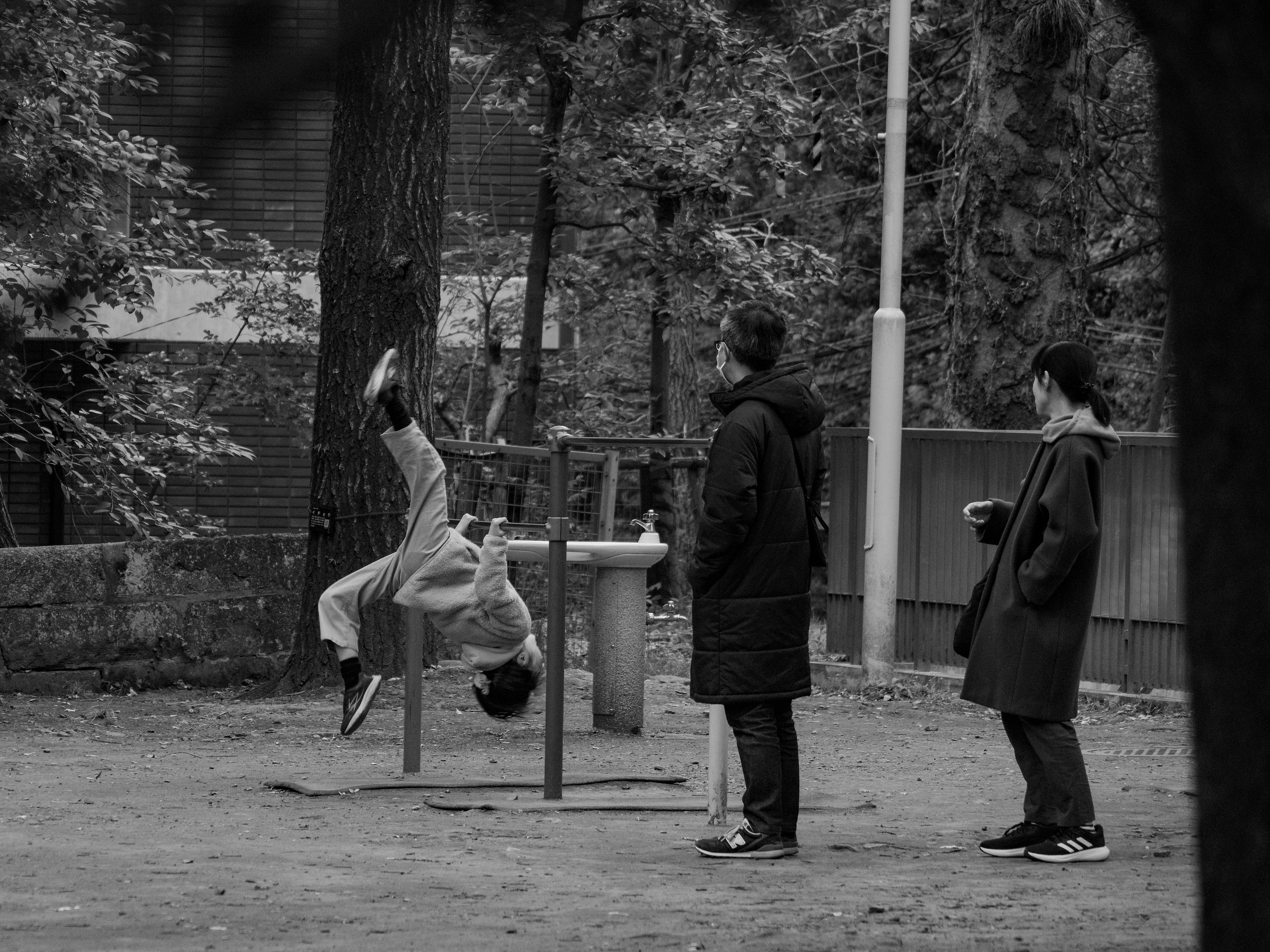 Child hanging upside down on playground equipment with two adults observing