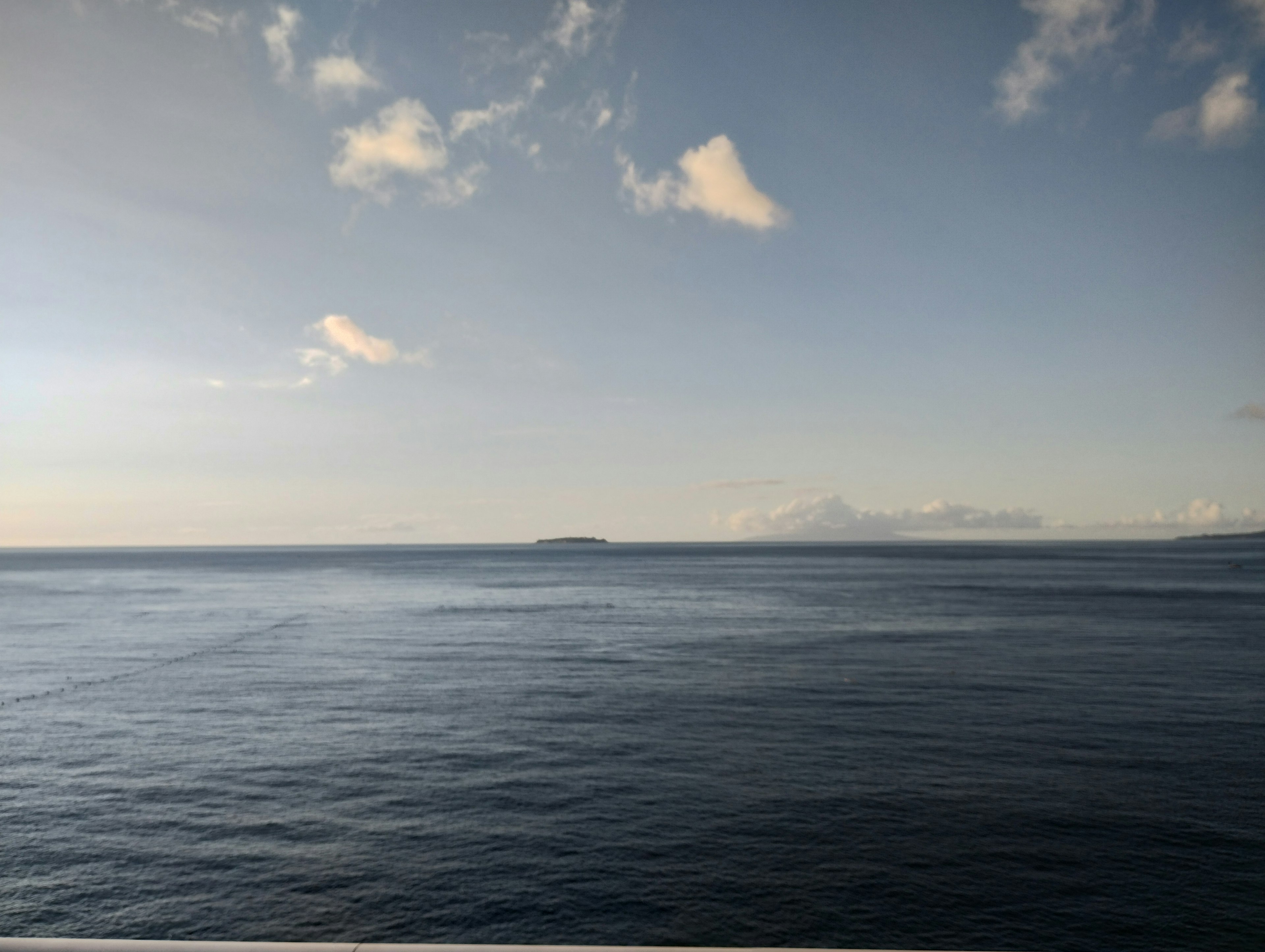 Pemandangan laut tenang dan langit biru dengan pulau di kejauhan