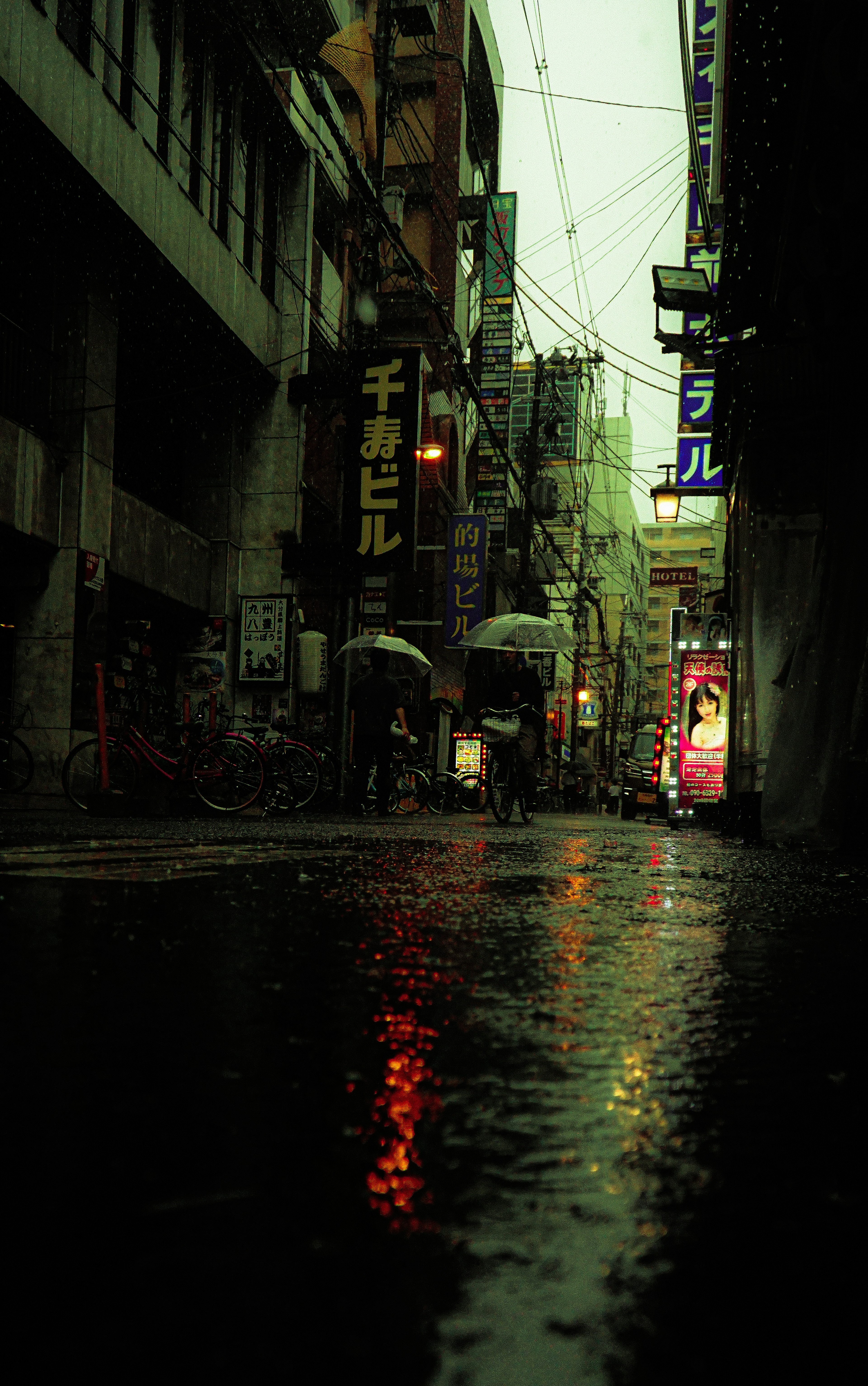 Rain-soaked street scene with people holding umbrellas, neon light reflections, moody atmosphere