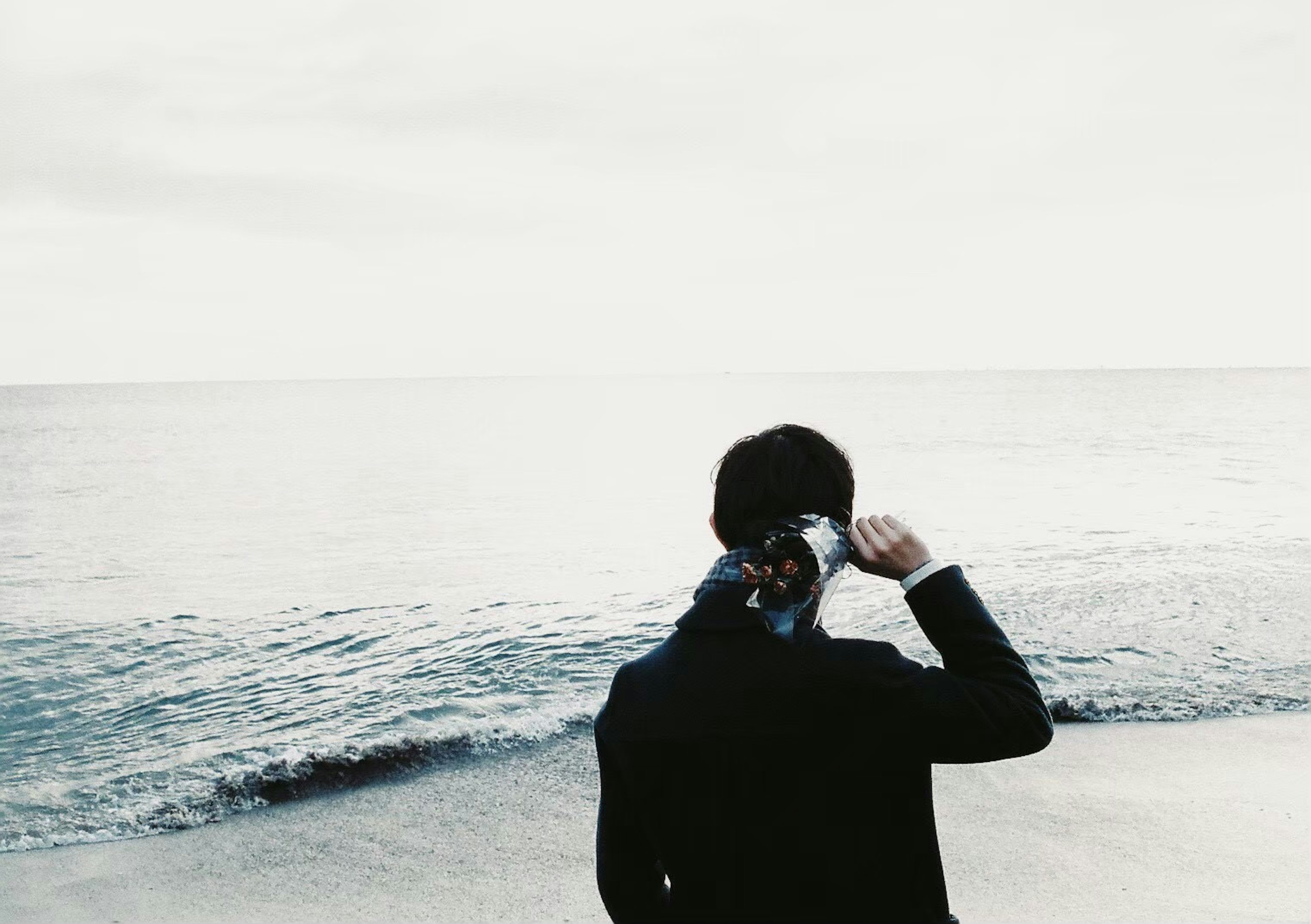 Un homme se tenant sur la plage tenant une écharpe regardant la mer