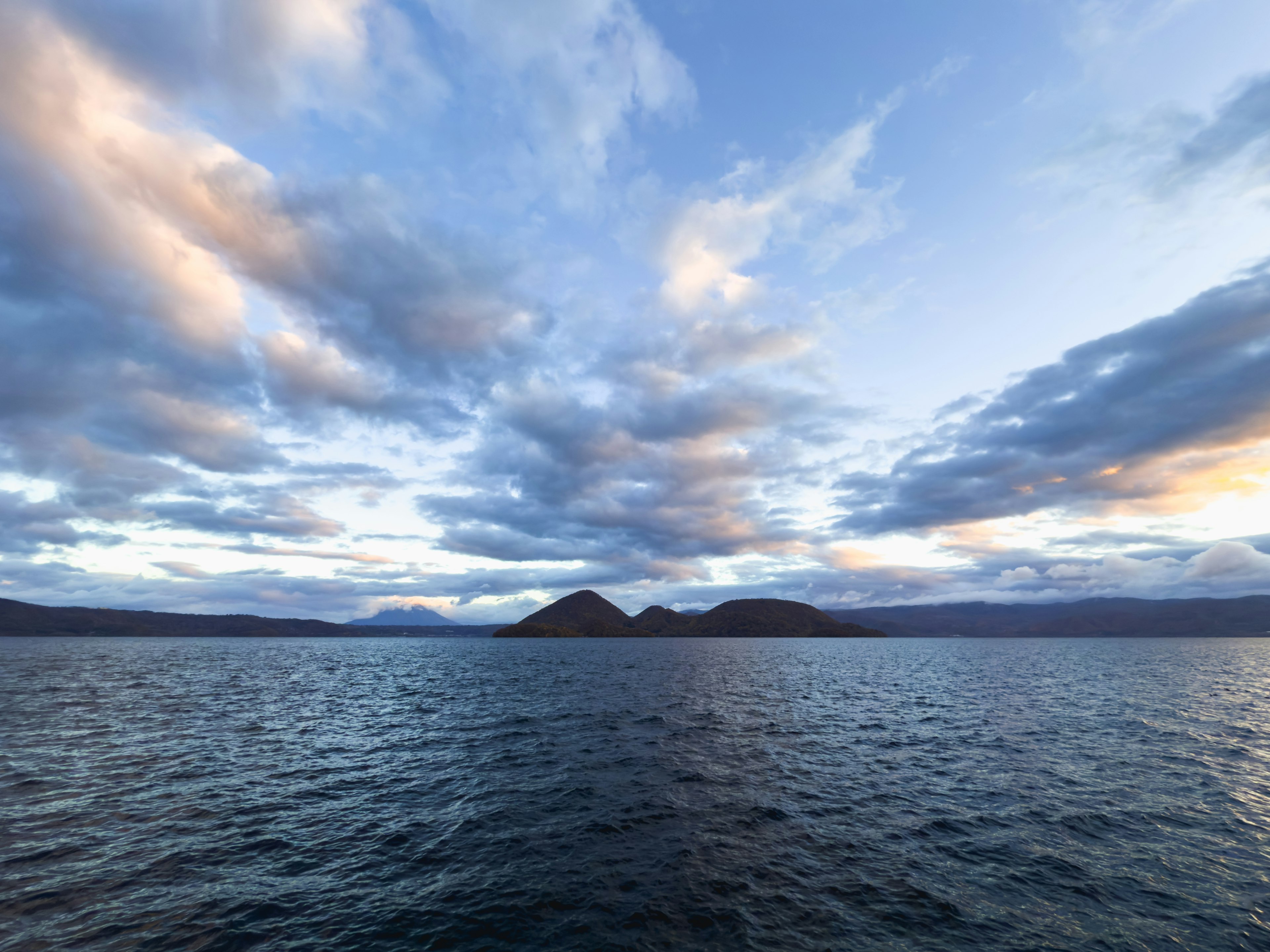 Scenic view of blue water and expansive sky with clouds sunset light illuminating mountains