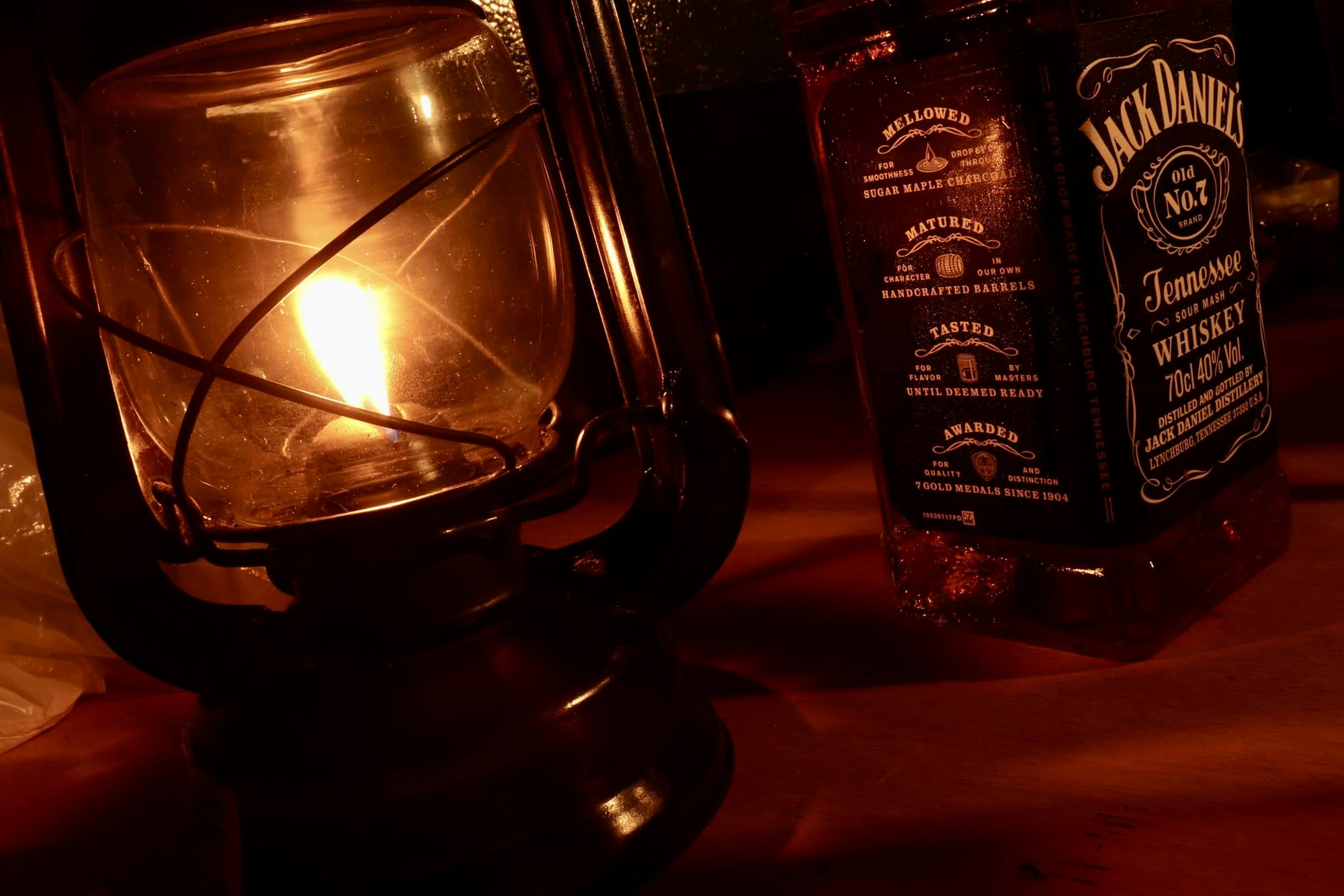 Una linterna que emite una luz cálida junto a una botella de whisky Jack Daniel's en un ambiente acogedor