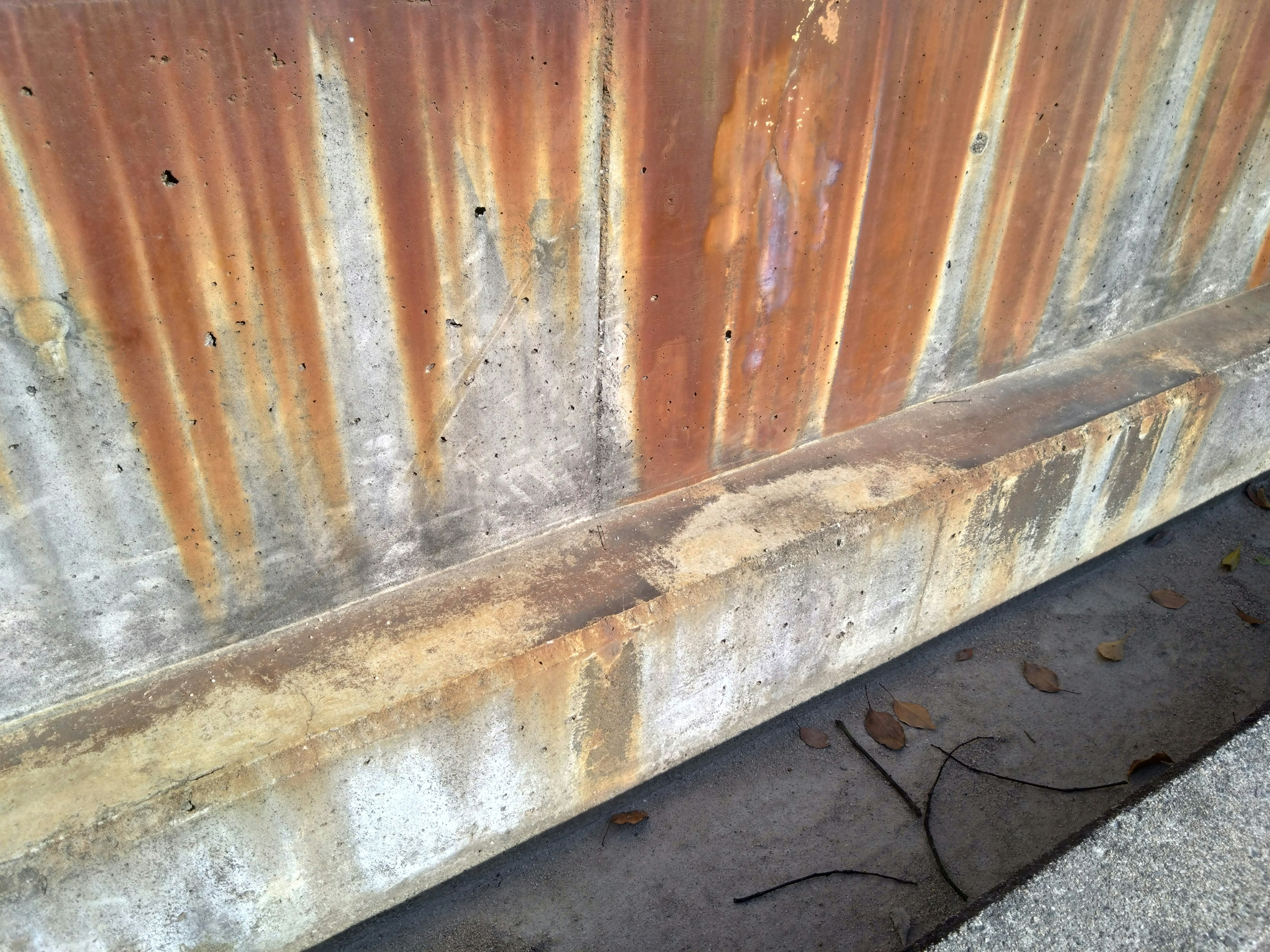 Rusty metal wall with concrete base showing distinct colors and textures