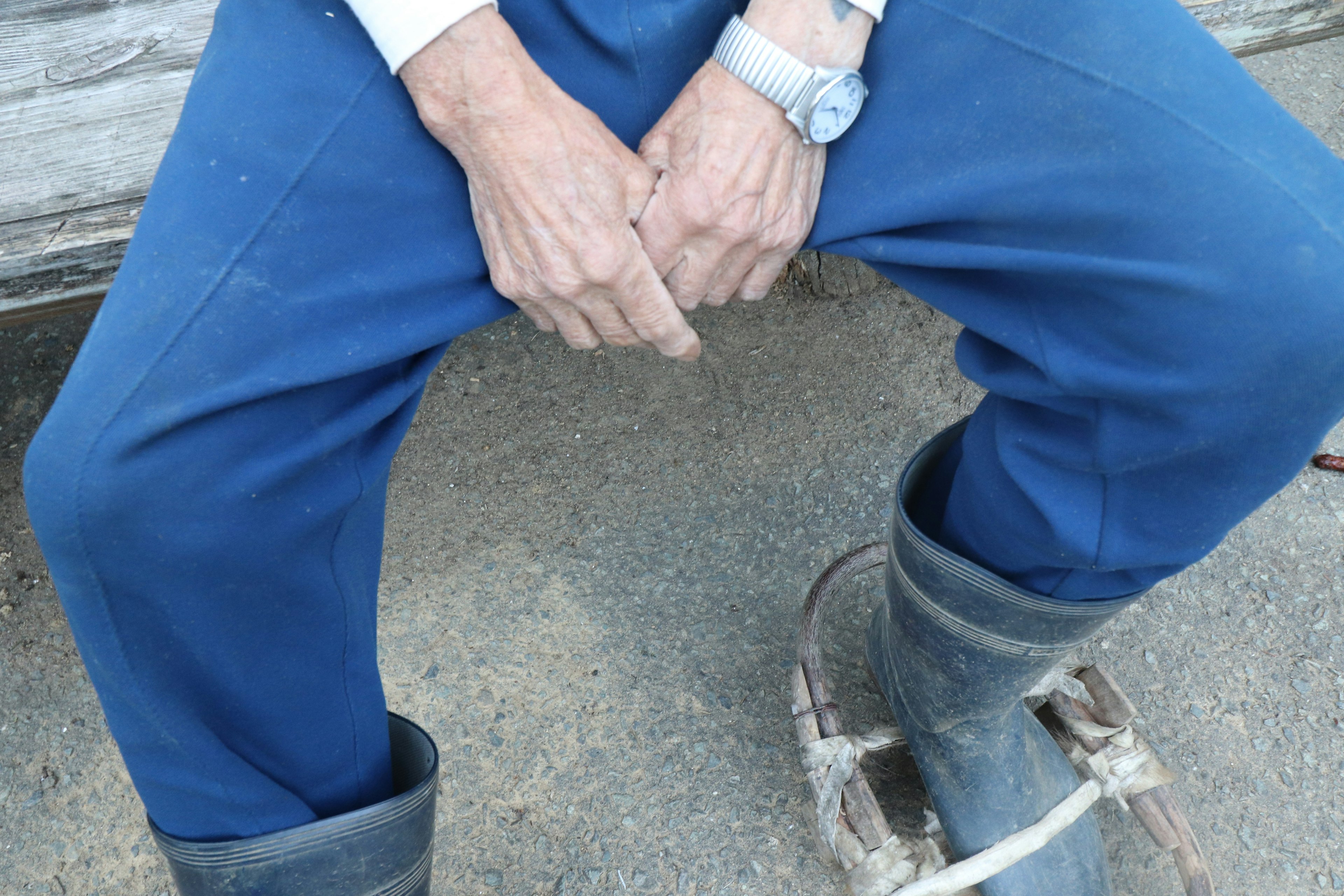 Primer plano de las manos de un hombre descansando sobre sus pantalones azules mientras usa botas de goma